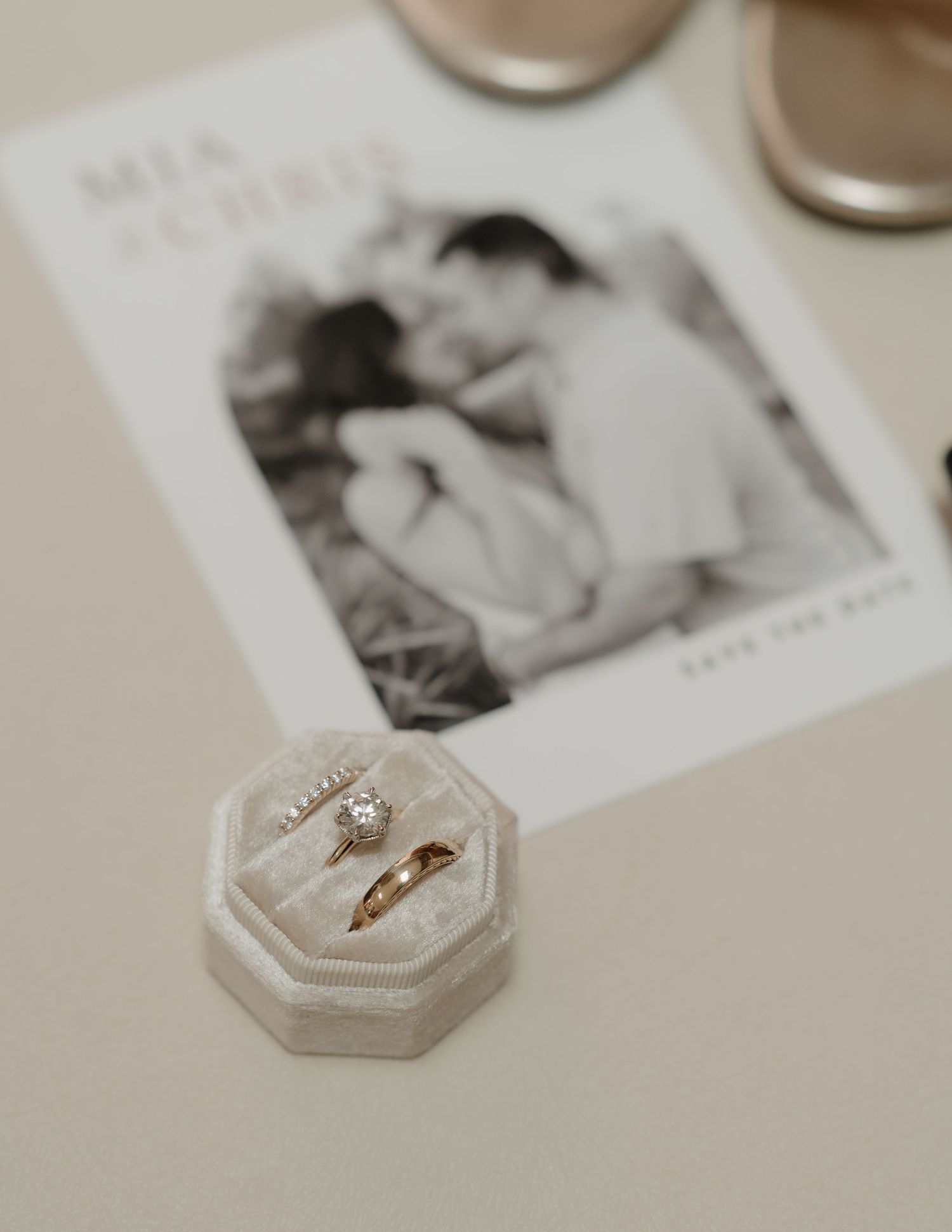 Gold wedding rings in a velvet box beside a save-the-date card reading Mia and Chris on a neutral background.