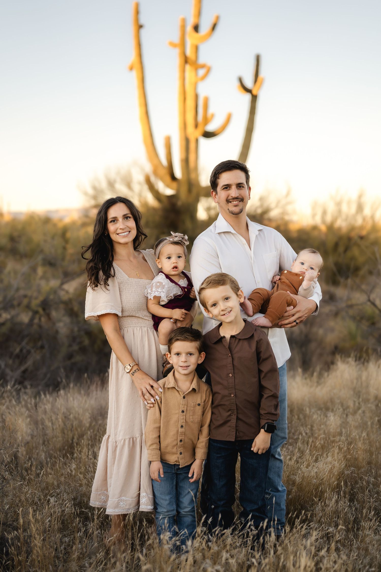 Family portrait at sunset with saguaro cactus in desert landscape wearing neutral colors.
