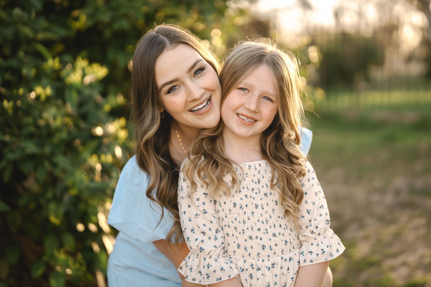 Two people embracing and smiling outdoors with green foliage background.