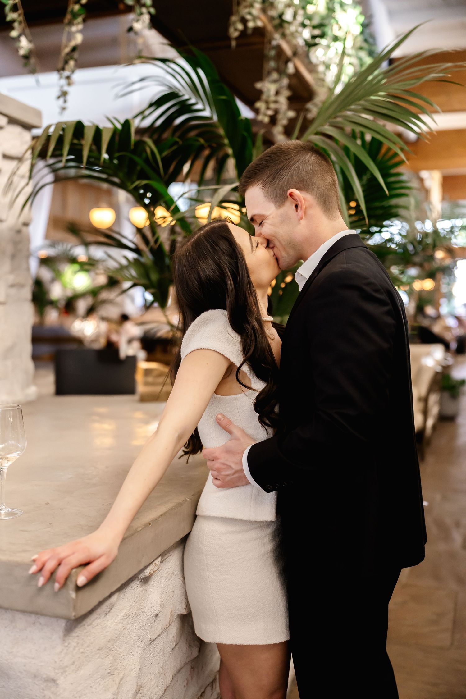 Couple sharing romantic moment near stone wall with tropical plants in upscale venue.