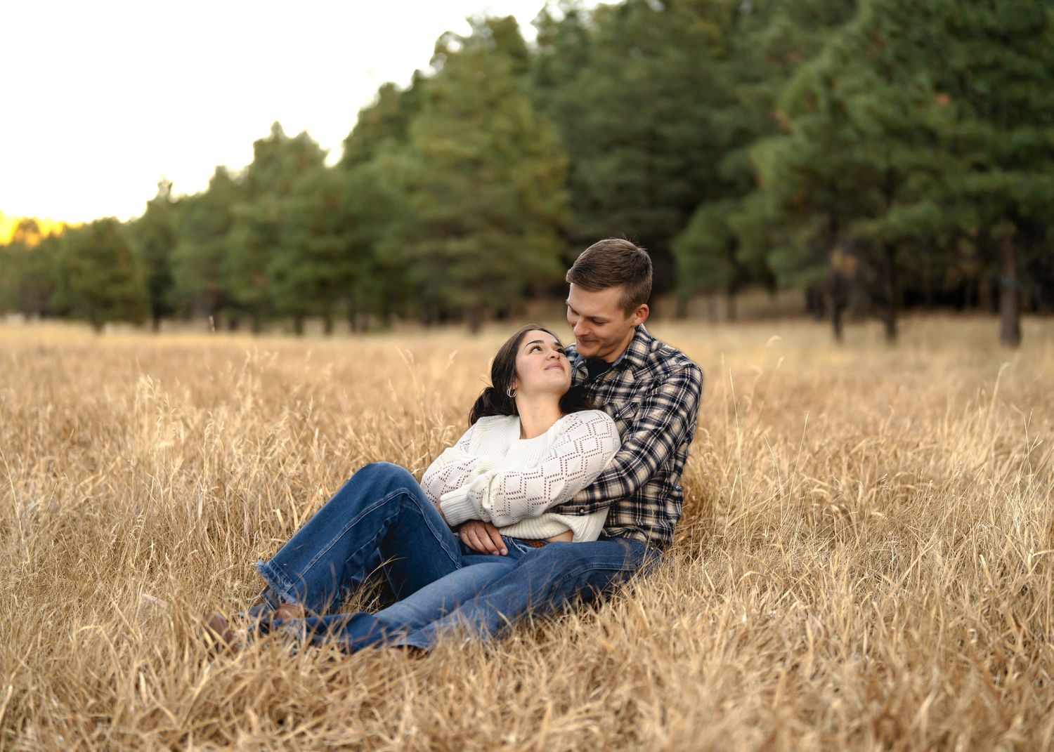 Couple relaxing together in tall golden grass during autumn sunset photography session.