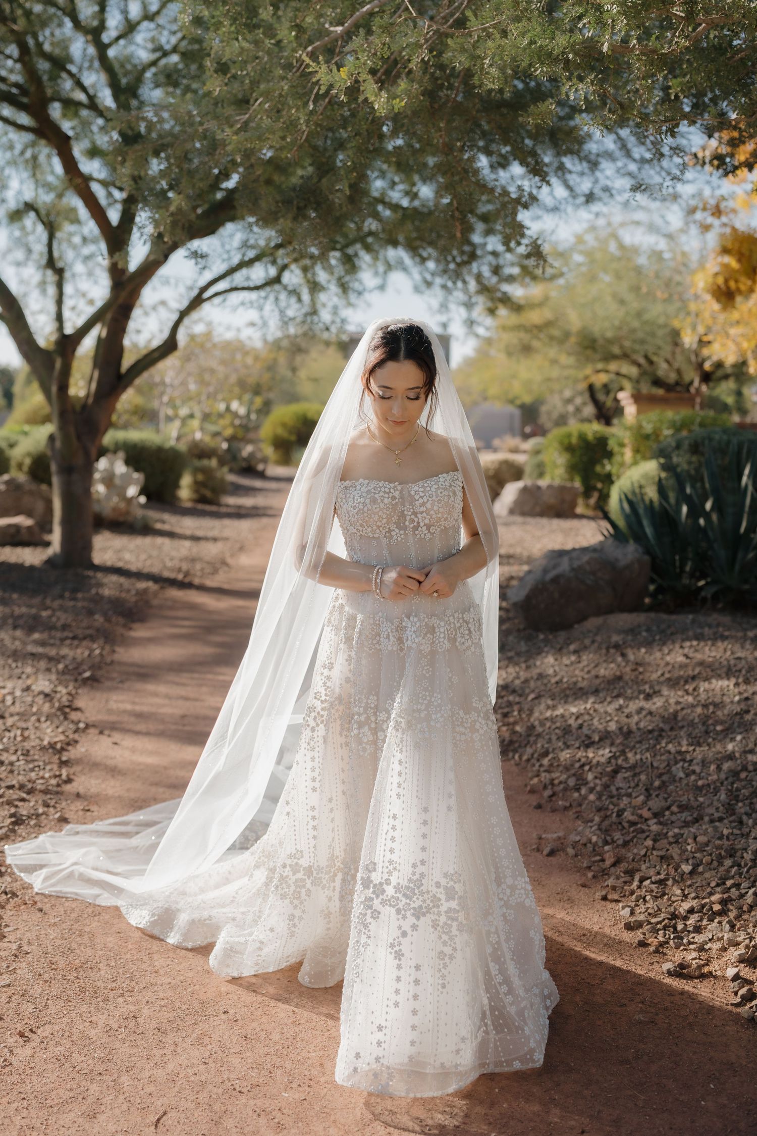 A flowing white wedding dress with delicate details is photographed in a desert landscape with scattered trees.