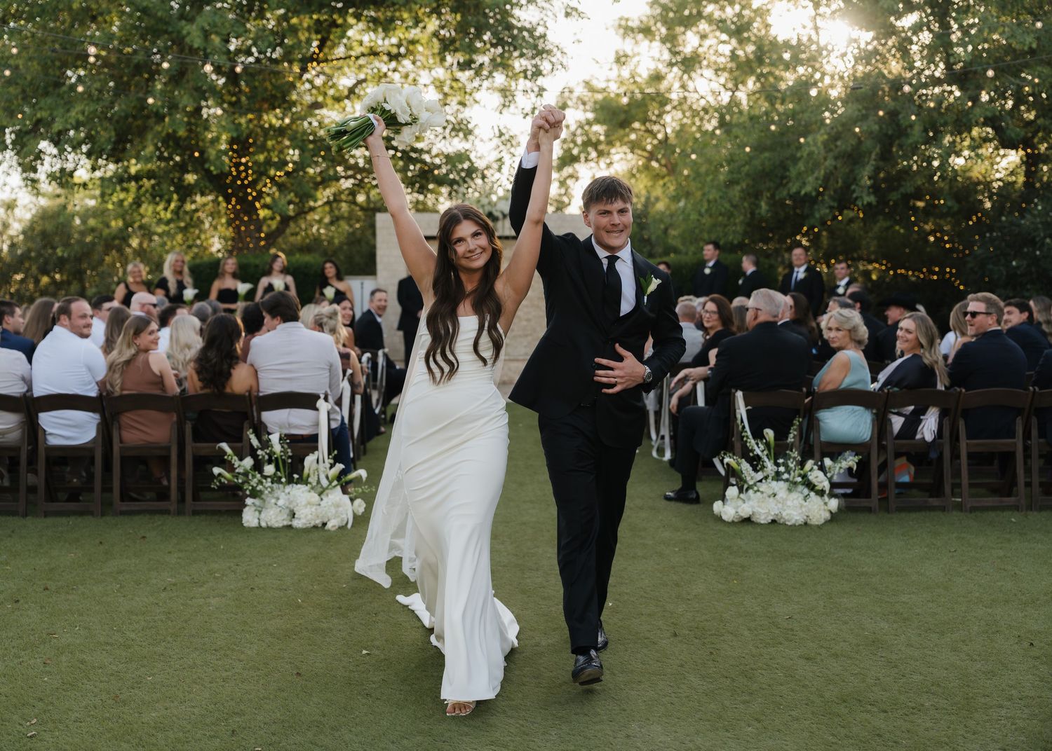 Joyful bride and groom celebrate recessional on lush green lawn at elegant outdoor wedding reception.