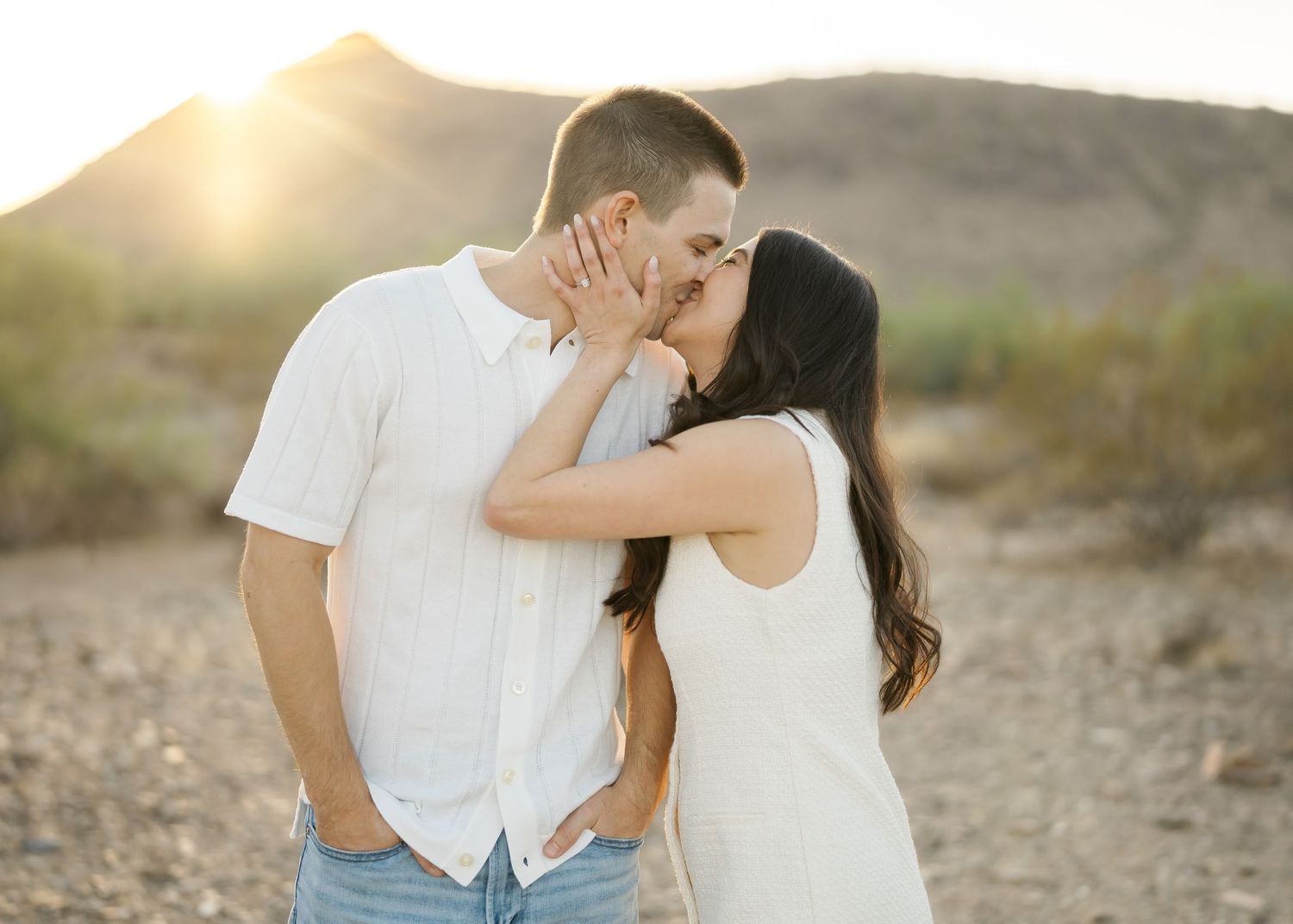 Couple embracing against golden desert landscape during sunset photoshoot.