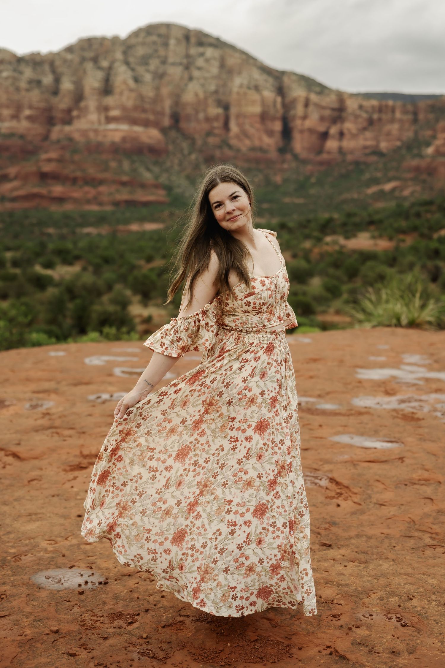 A floral dress flows in the wind against dramatic red rock landscapes.