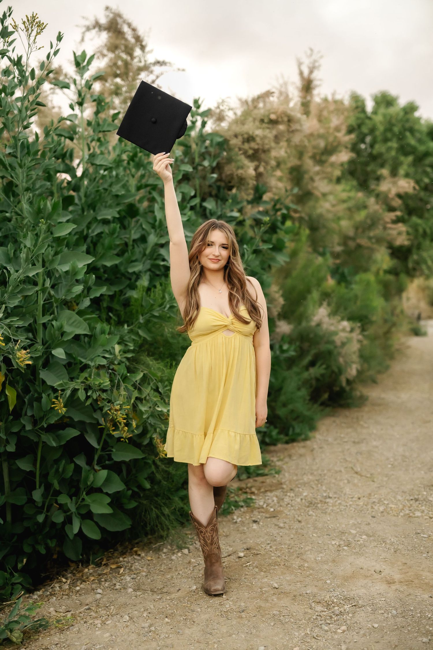 Someone in a yellow dress celebrates on a gravel path surrounded by lush greenery.