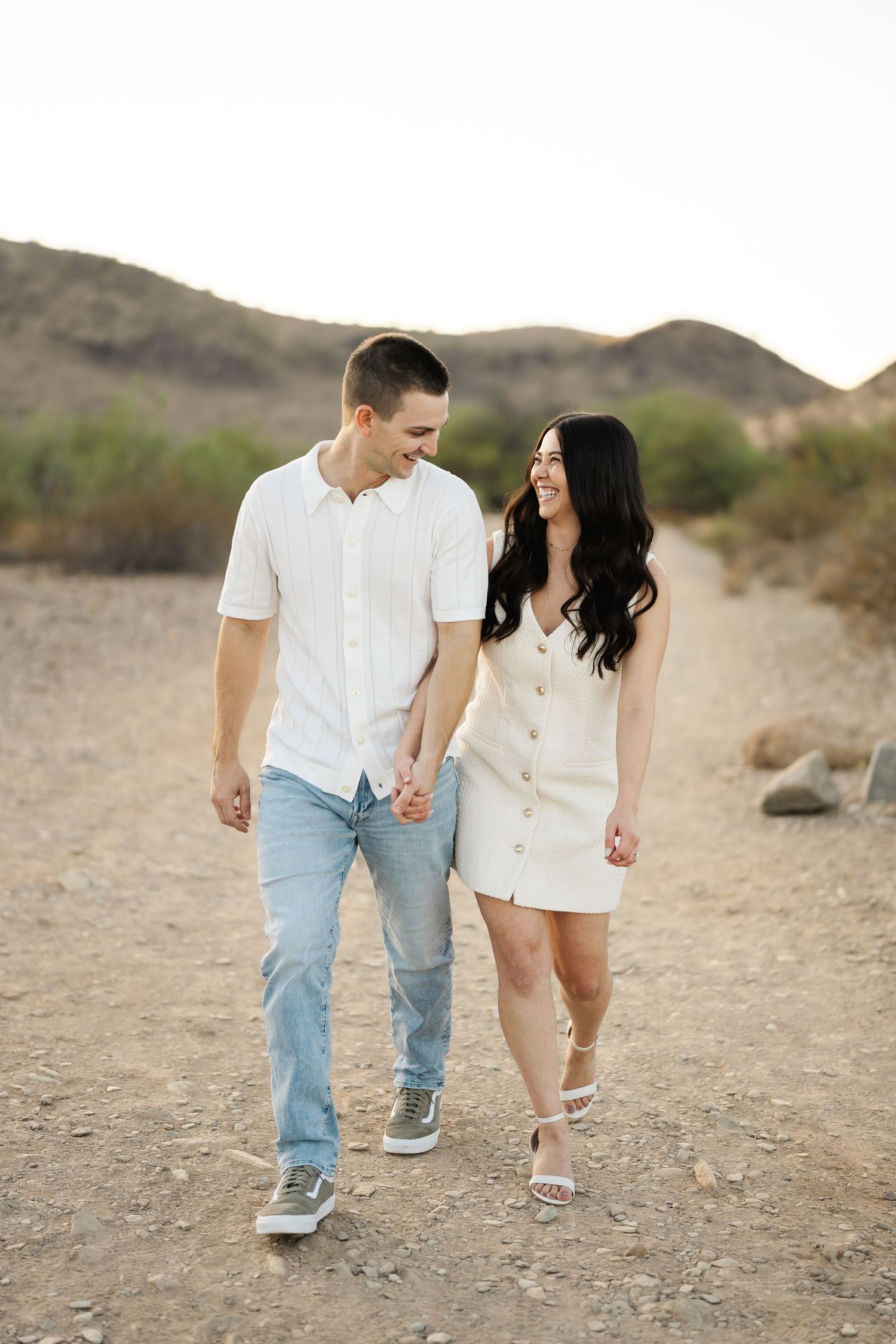 Couple in white outfits walking hand in hand through desert terrain.