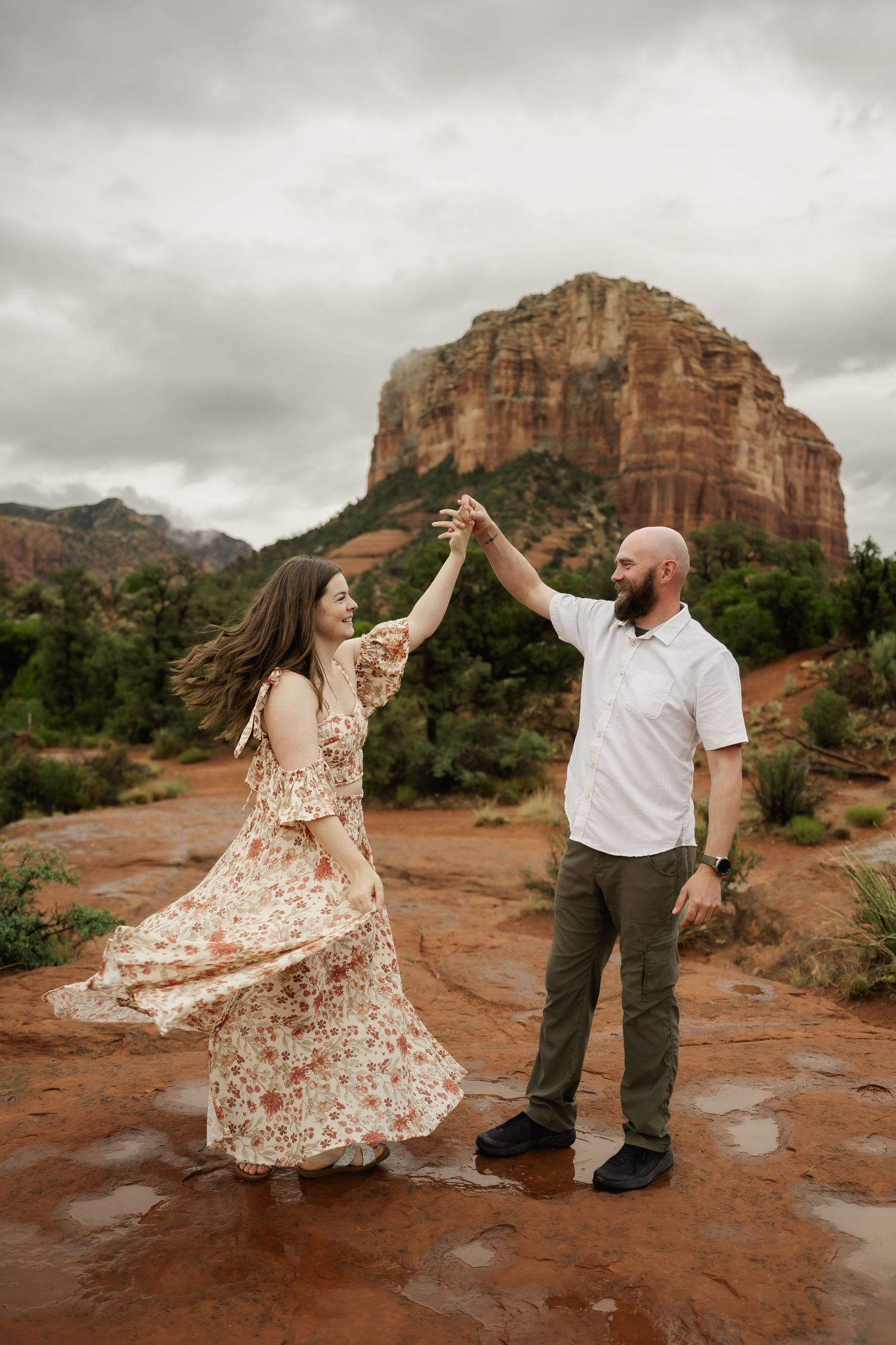 A couple dances together against the stunning backdrop of red rock formations in Sedona at sunset.