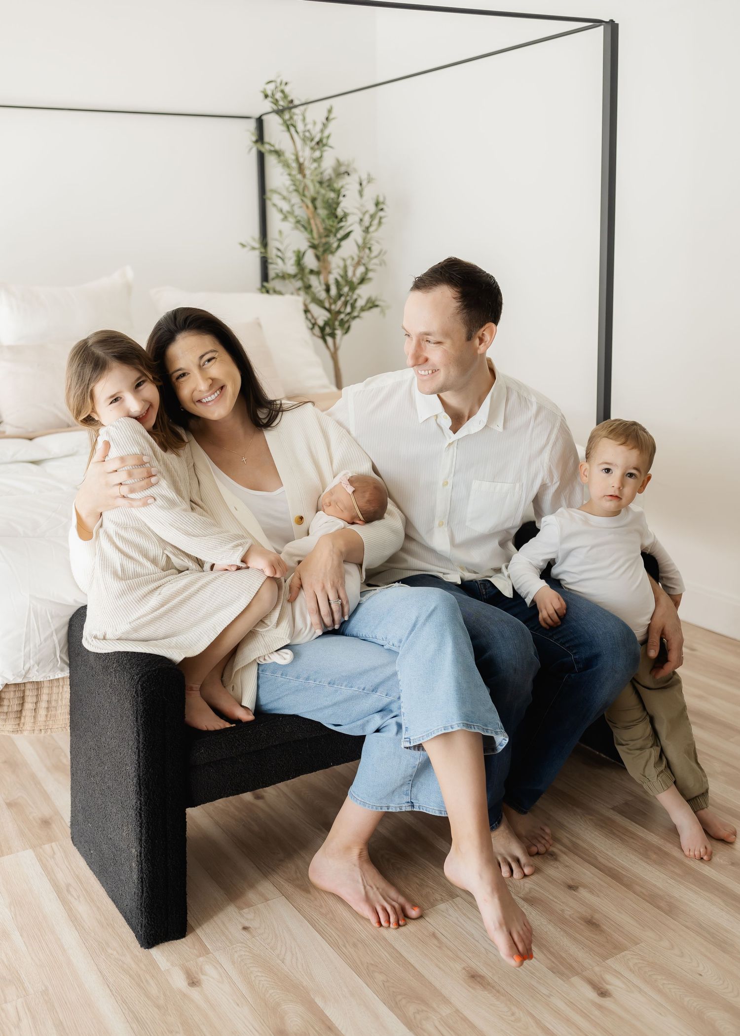 Family members lounging together on a dark sofa against white walls with decorative greenery.