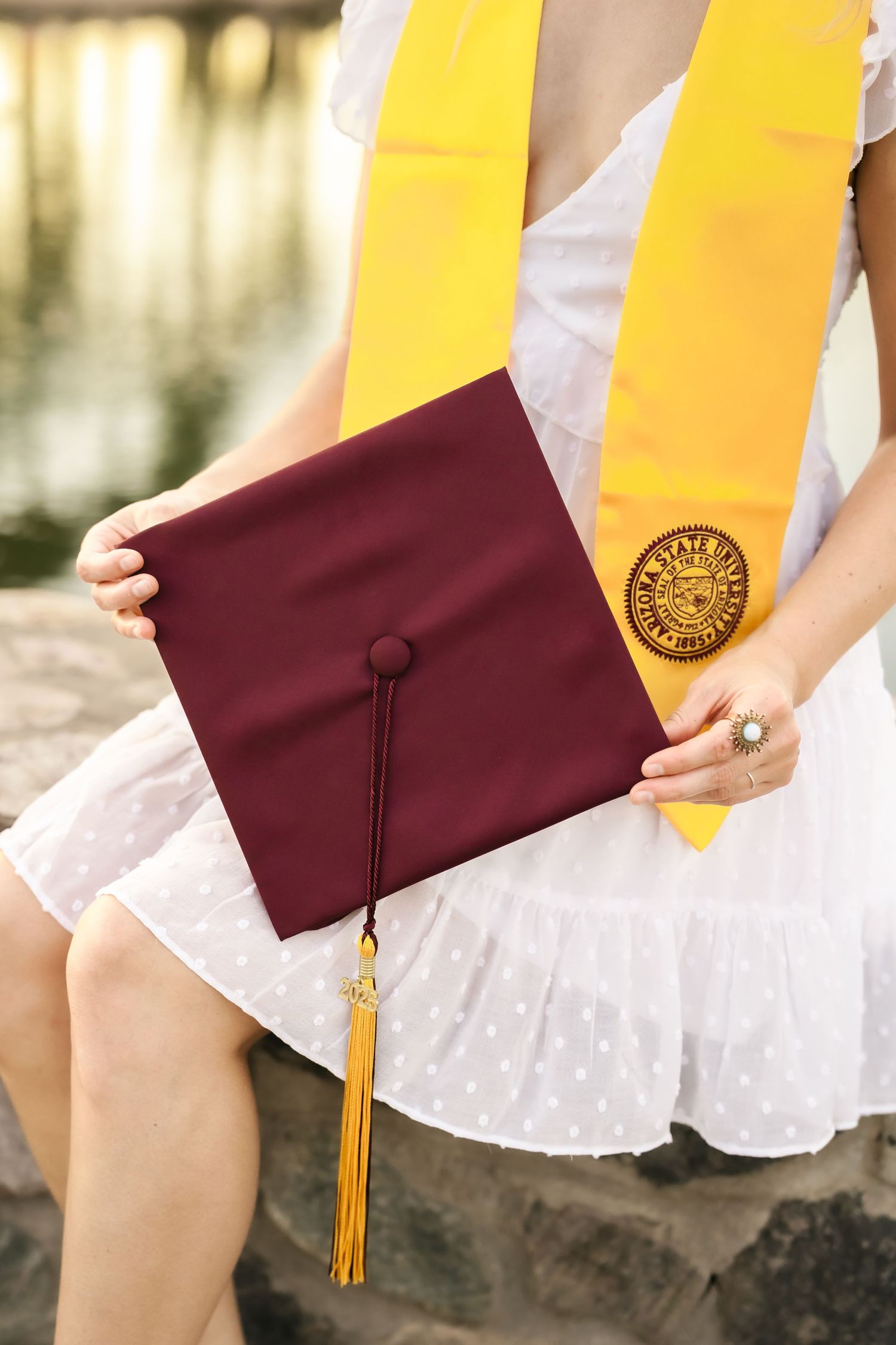 Close-up of maroon graduation cap and gold tassel against white dress.