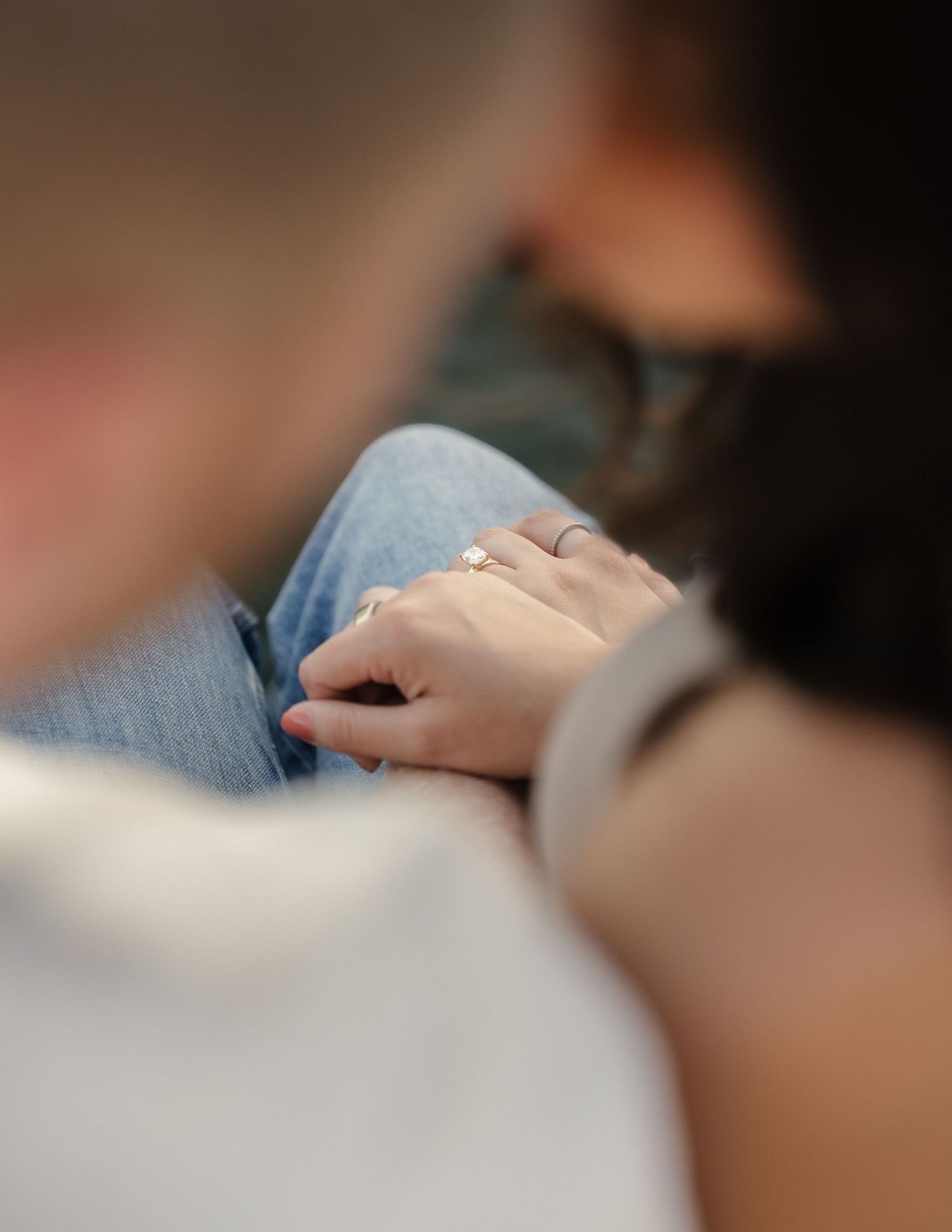 Close-up of a woman's hand with an engagement ring resting on a man's arm, symbolizing love and commitment.