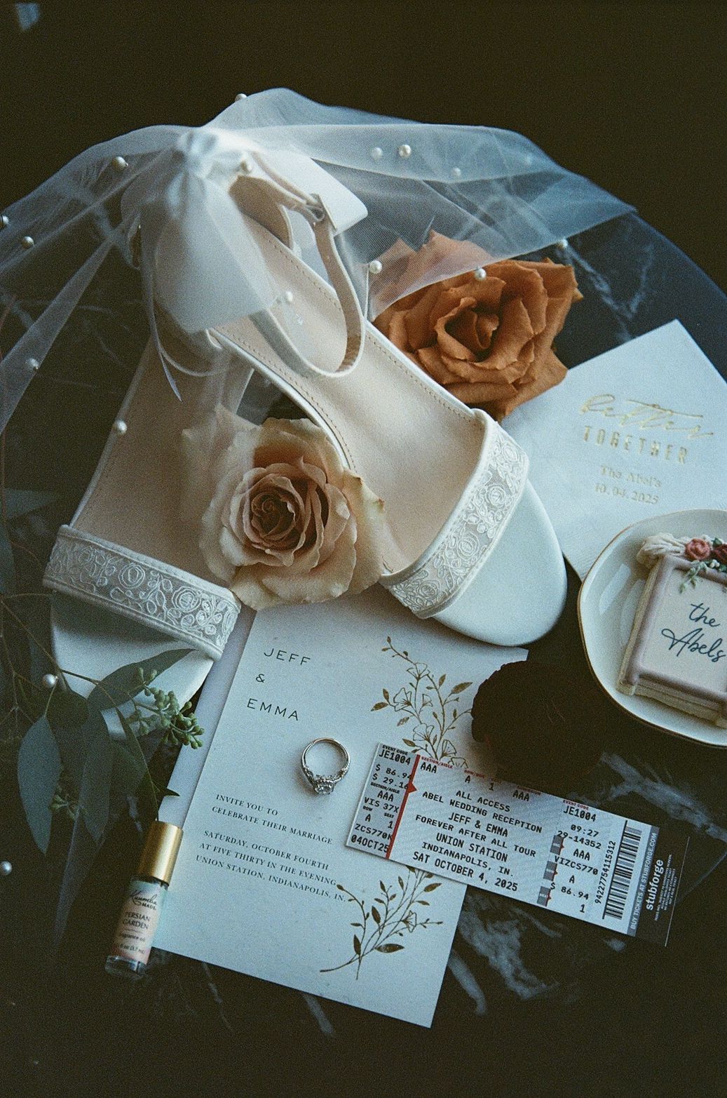 White bridal heels, wedding invitation for Jeff and Emma, engagement ring, roses, and veil arranged in a flat lay display.
