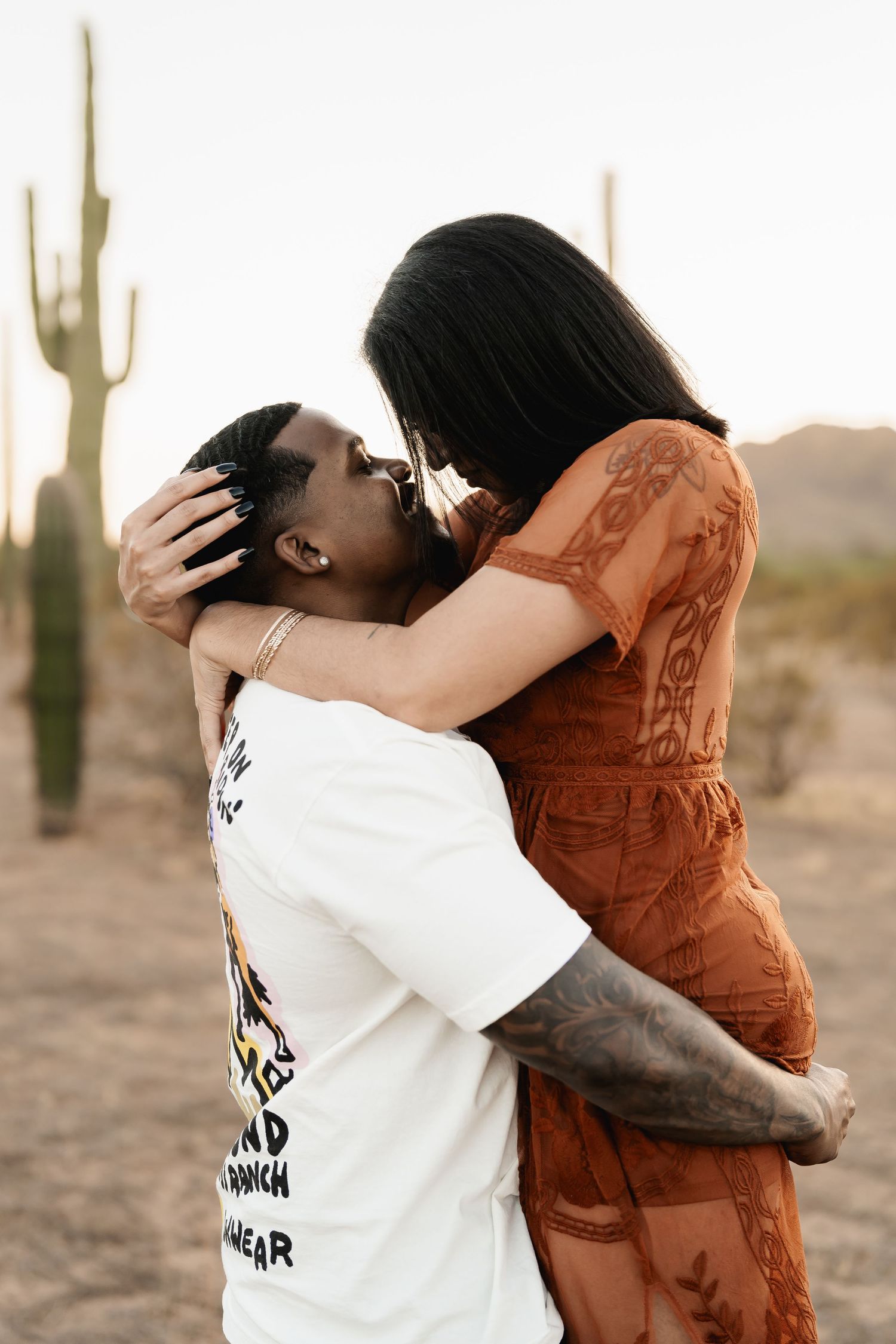 Intimate embrace captured at sunset with saguaro cactus silhouette in background.