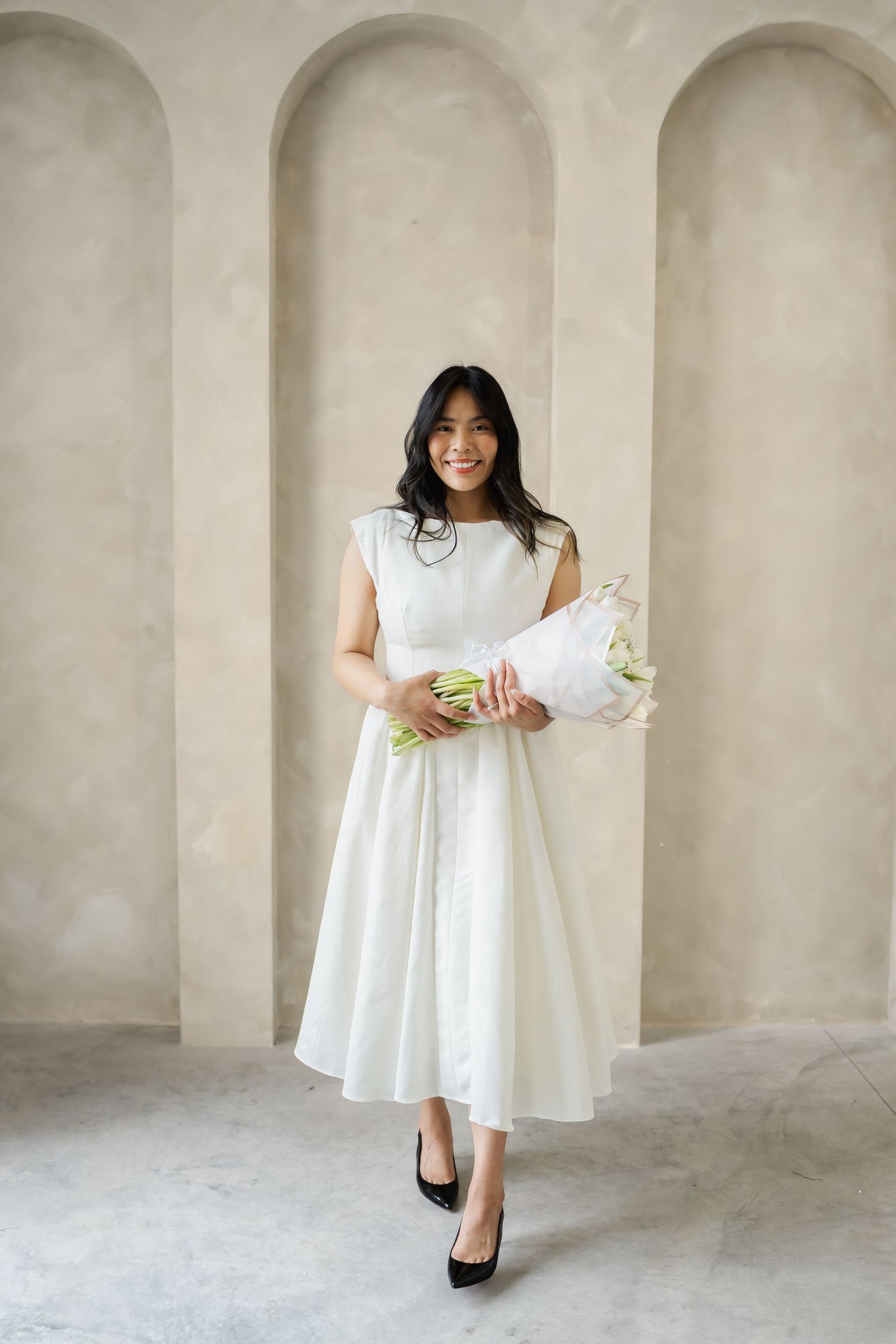 Person in white dress posing in architectural setting with arched doorways.