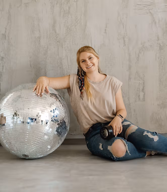 Kayla Koch Photo poses for branding photos on a disco ball in a photography studio.