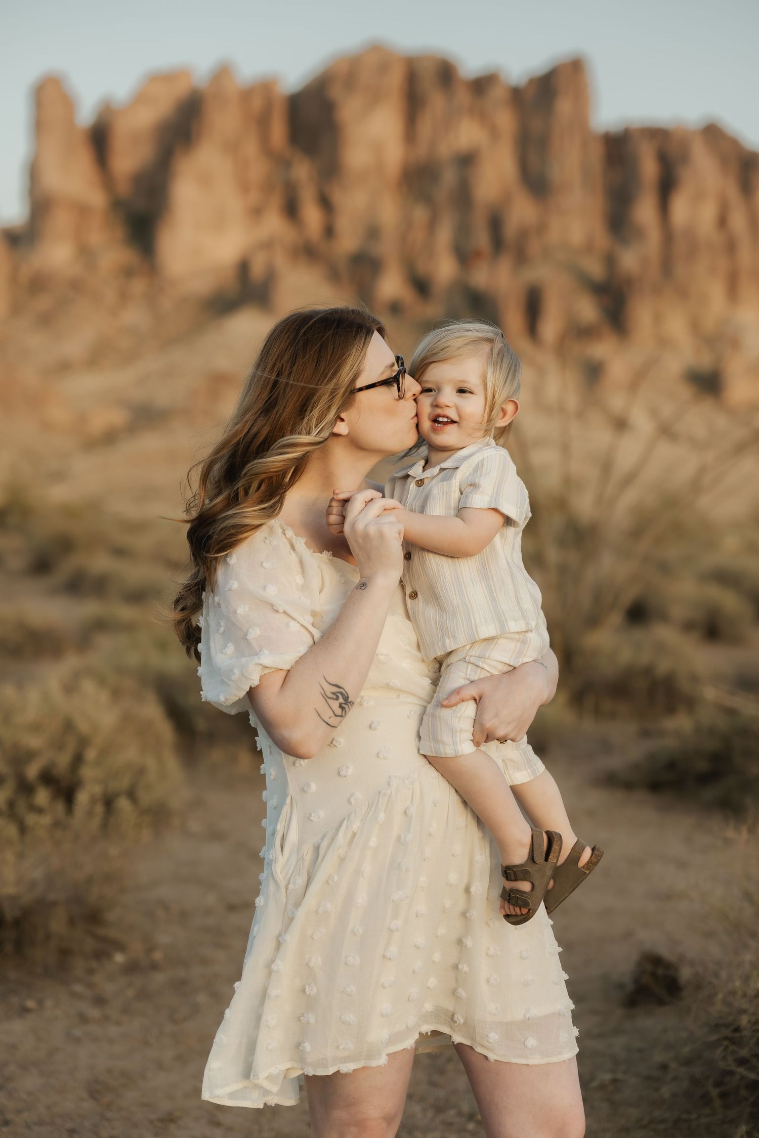 Mother and child in white dresses posing together against dramatic desert rock formations.
