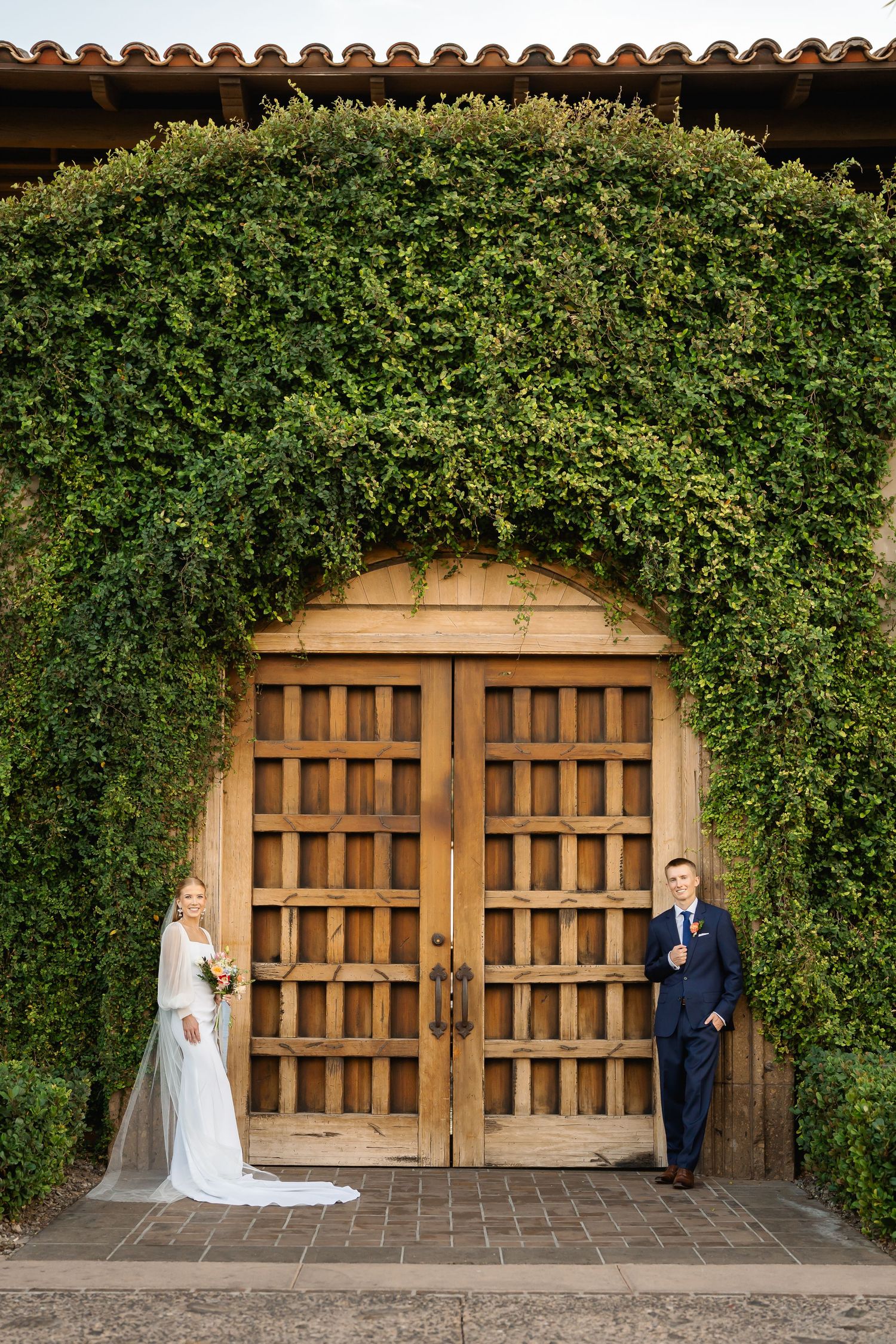 Wooden doors covered with lush green vines create a romantic backdrop for wedding photography.