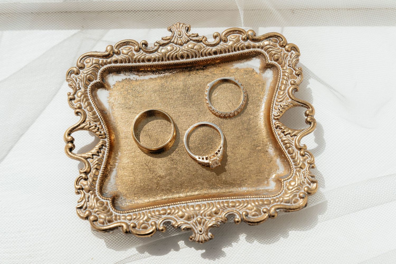 Ornate gold decorative trinket trays with baroque style borders displayed on white fabric.