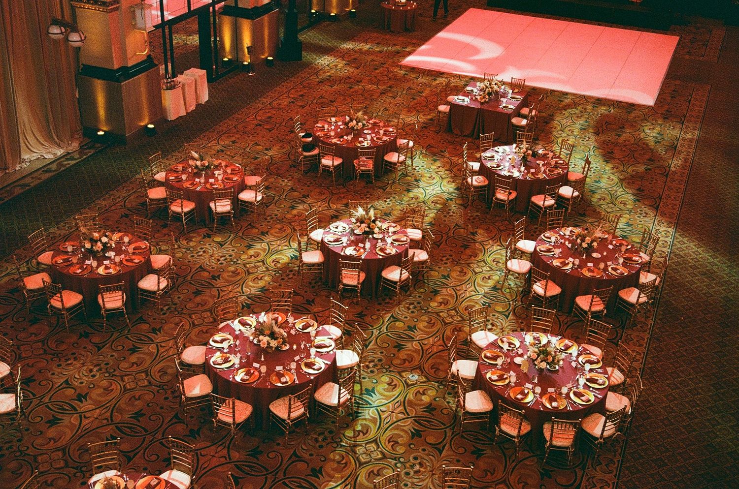 Aerial view of elegant wedding reception venue with round tables, floral centerpieces, and warm red ambient lighting.