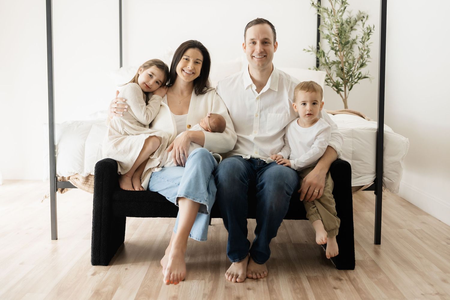 Minimalist indoor family portrait session on light wooden floor against white backdrop.