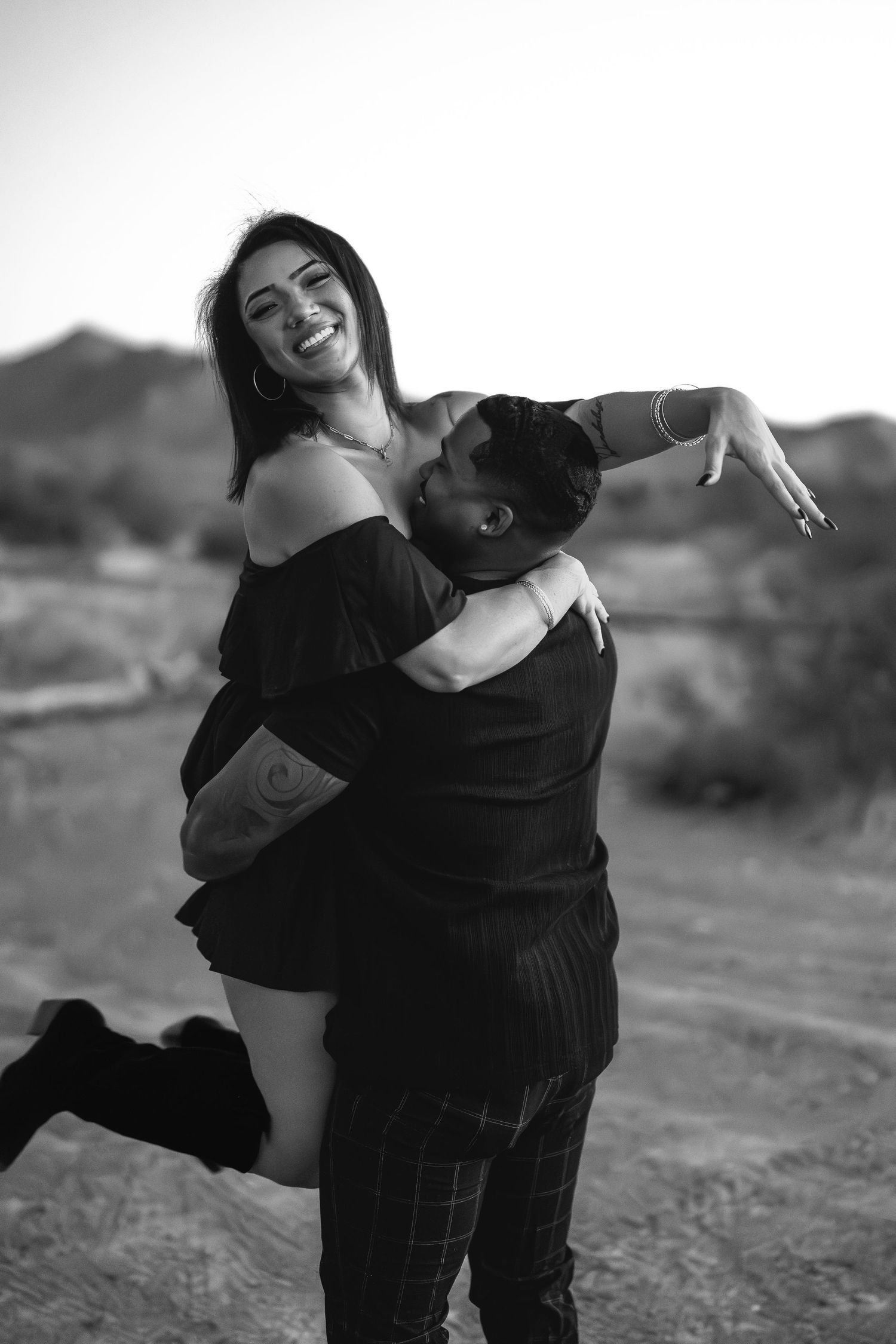 A joyful desert photoshoot showing a couple embracing in black and white.