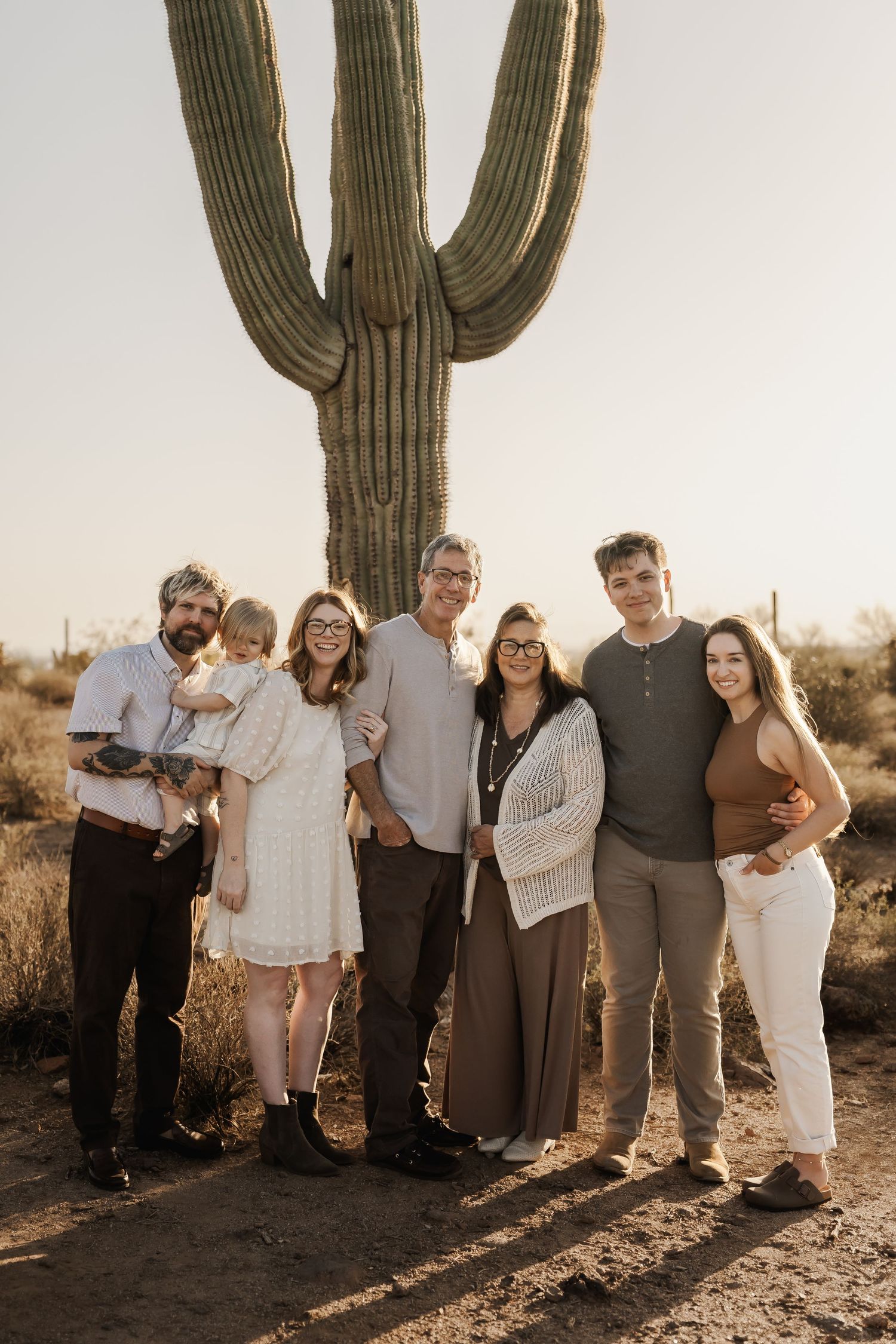 Extended family group photo in coordinated neutral outfits against desert landscape with saguaro cactus.