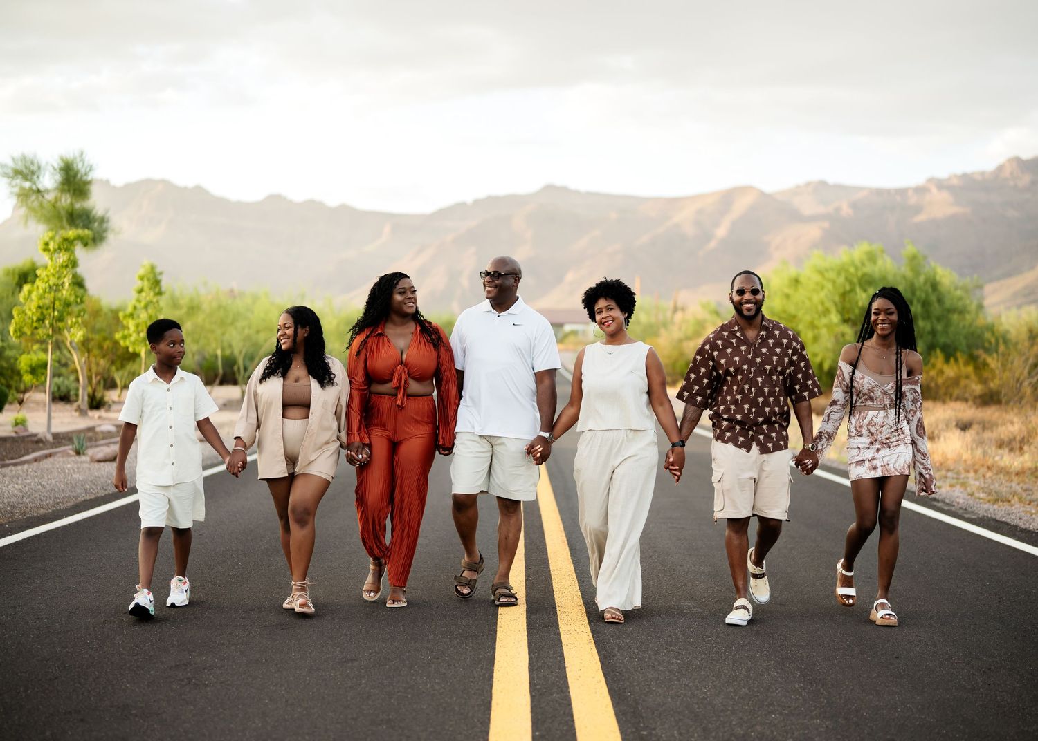 A diverse group of people walking down an empty desert road holding hands and wearing coordinated outfits.