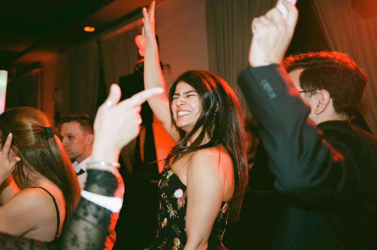 Woman smiling and dancing at a formal party event with guests celebrating in elegant attire.