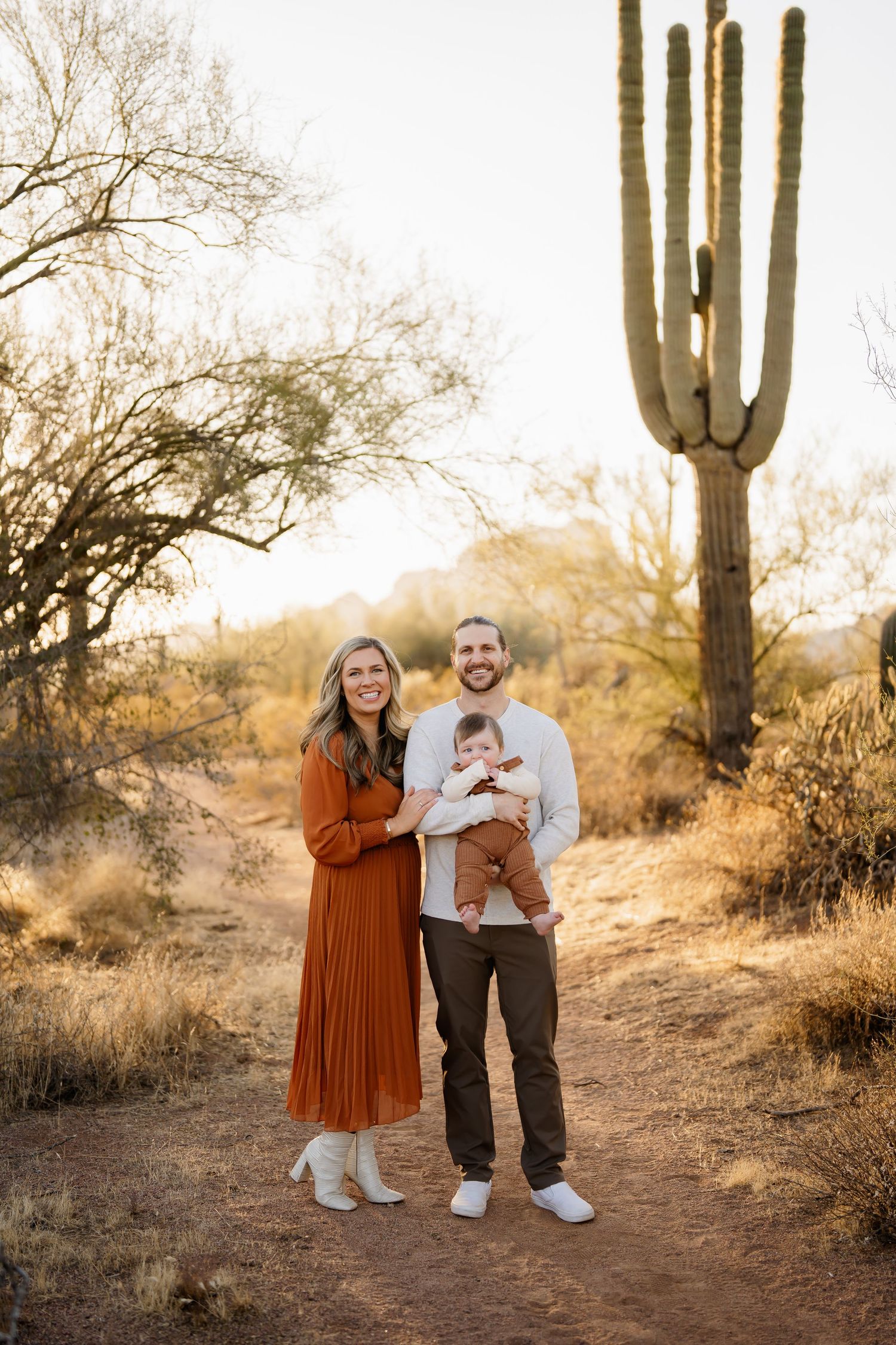 Family poses together on desert path with towering saguaro cactus in golden light.