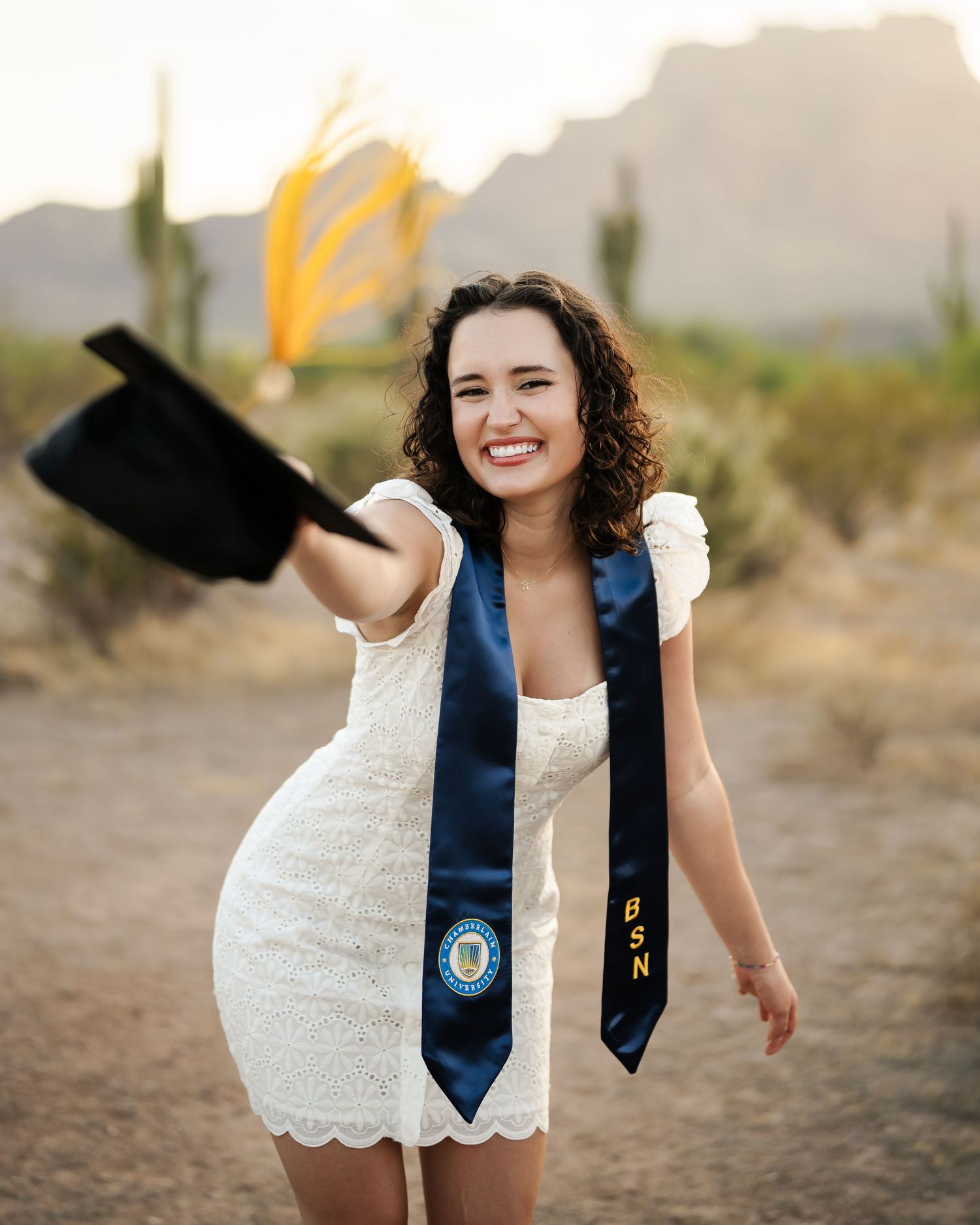 White dress and graduation stoles against desert landscape with saguaros.