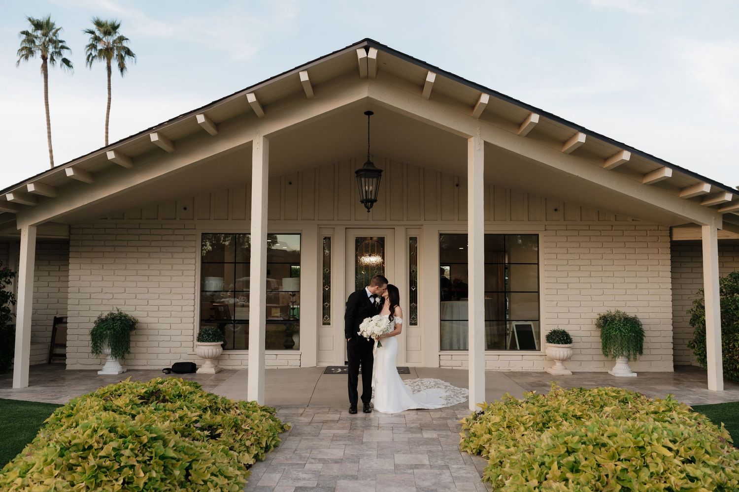 Modern beige event venue with palm trees and covered walkway in tropical setting.