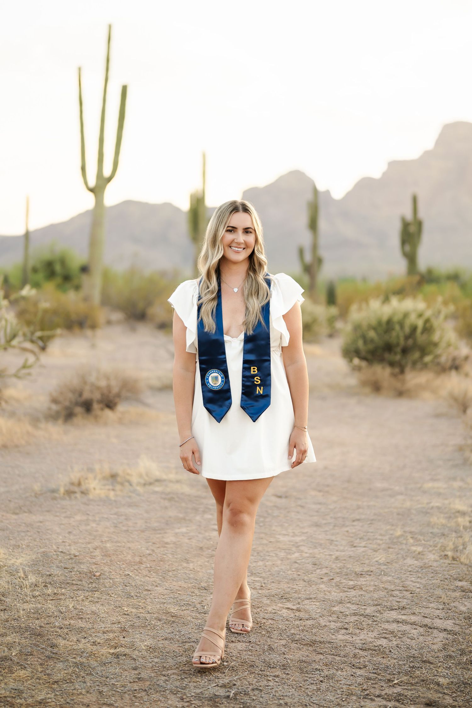 Graduate poses in desert setting with saguaro cacti and mountains in background.