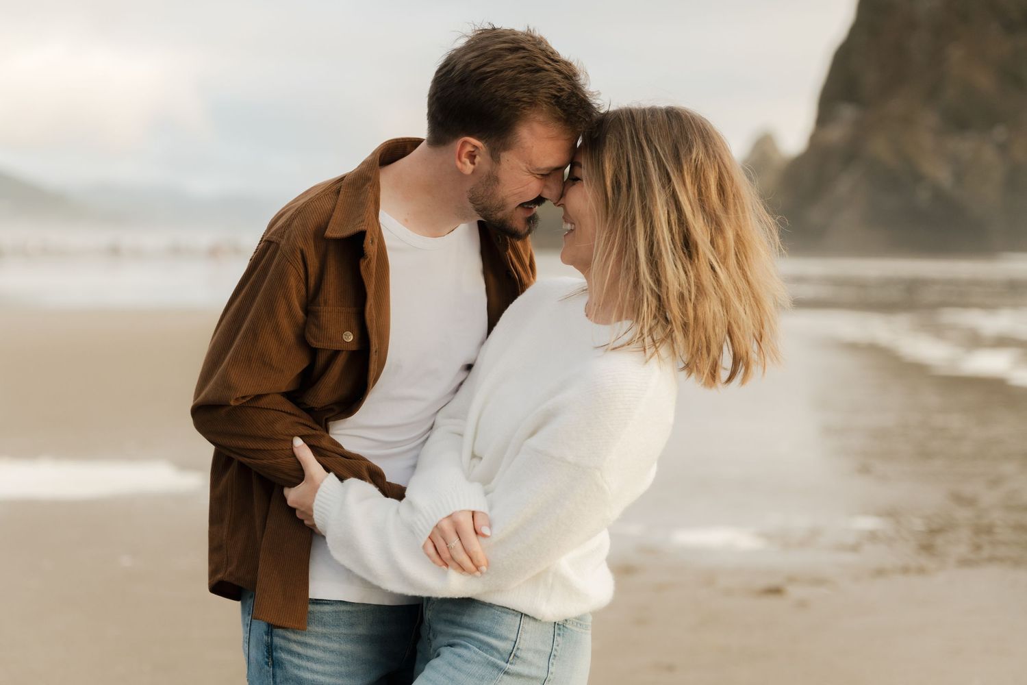Romantic couple embracing and sharing a tender moment on a scenic beach with dramatic rock formations.