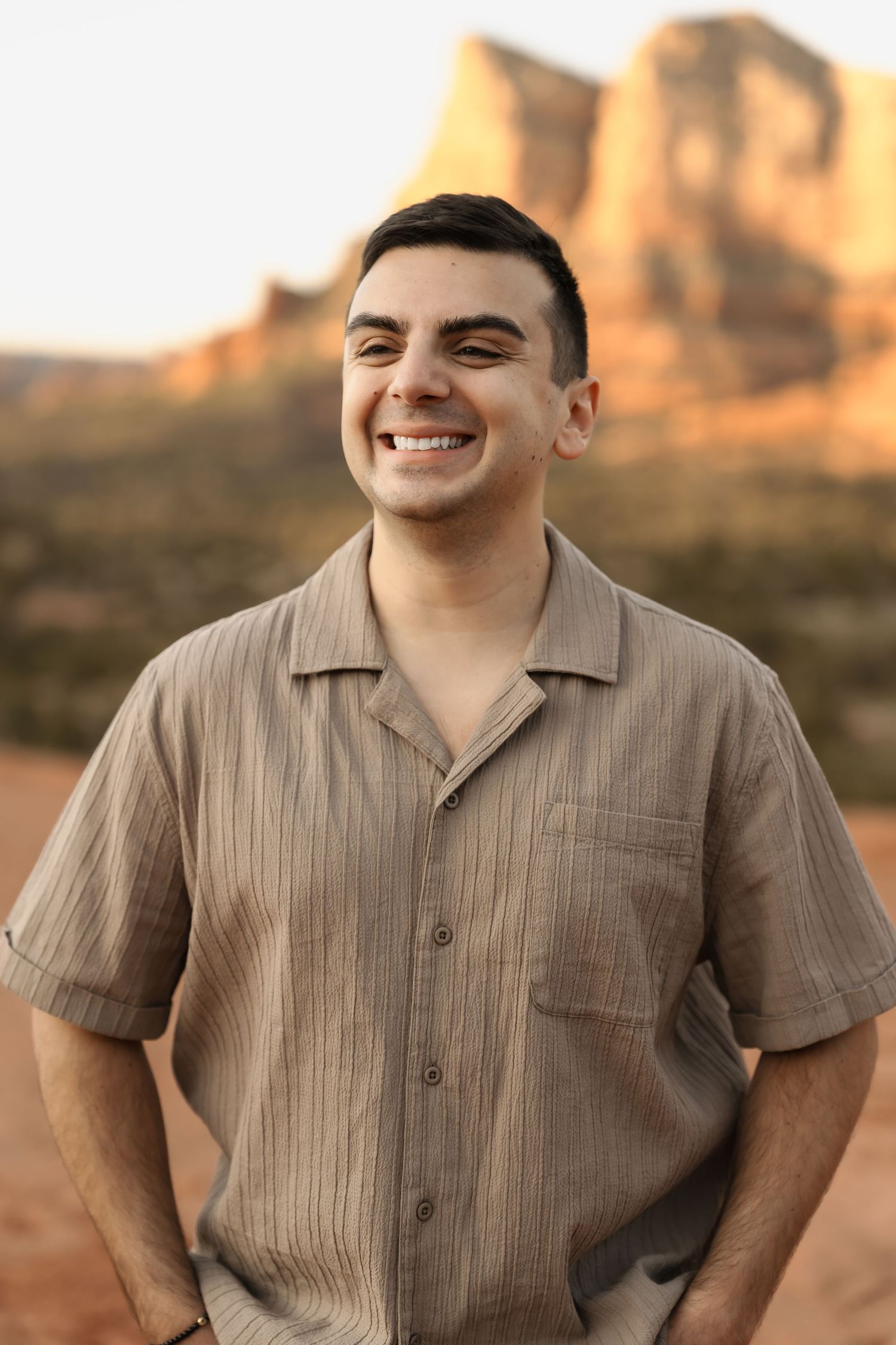 A person in a tan collared shirt smiles warmly in the desert sunlight.