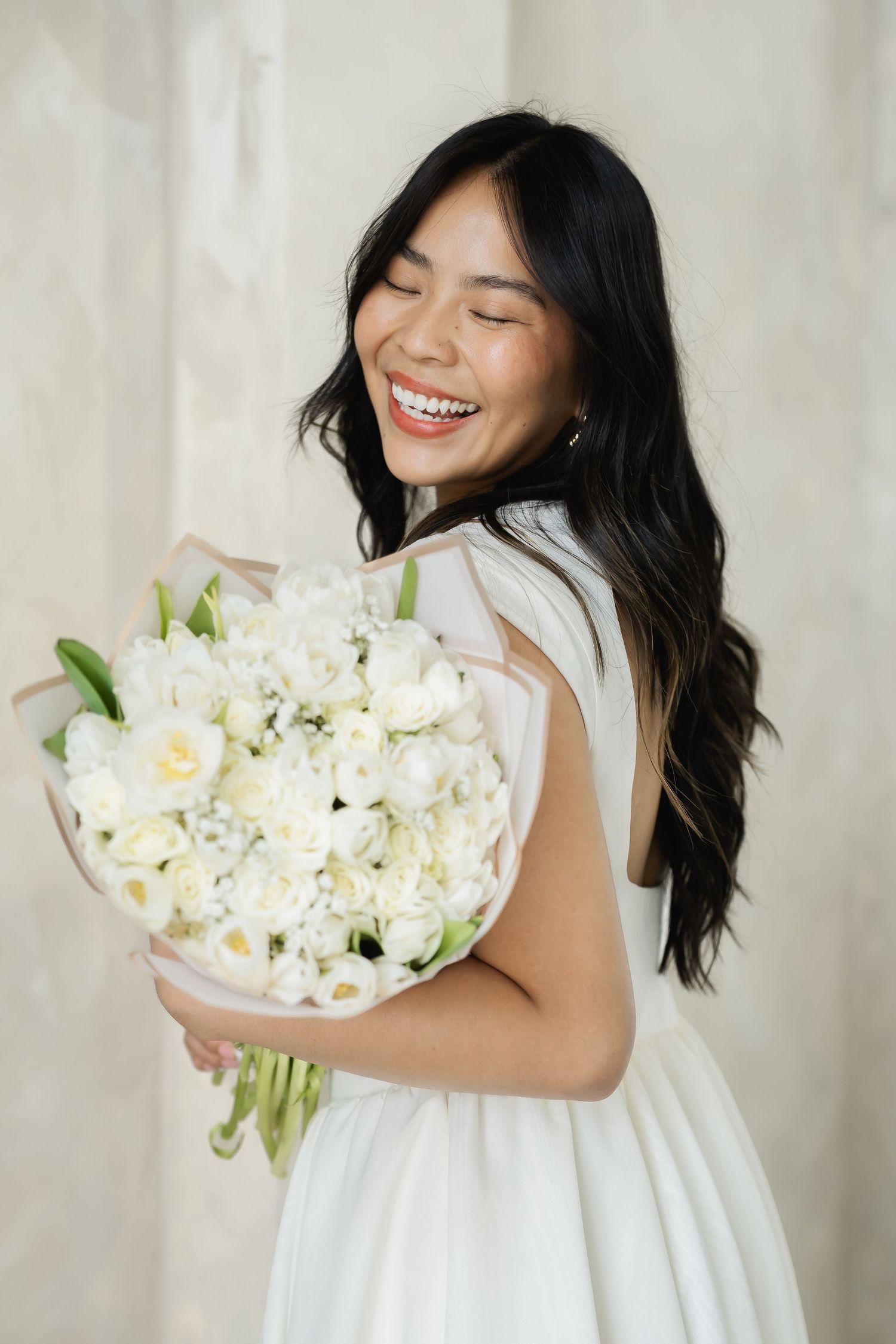 Person in white dress holding a large bouquet of white flowers against light background.
