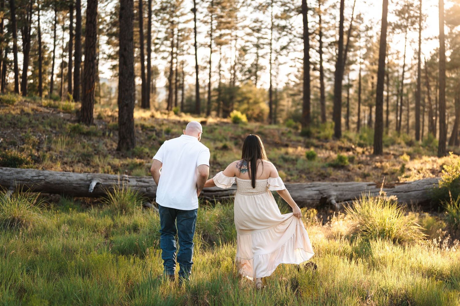 Golden hour engagement session in a pine forest with sunlight streaming through trees.