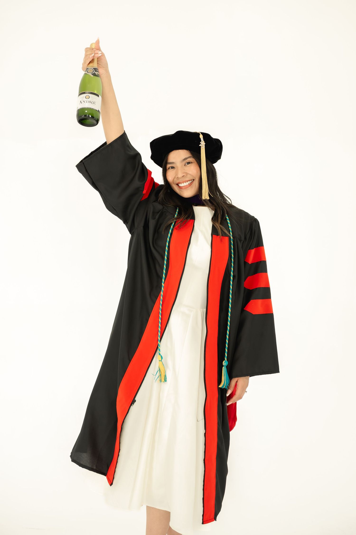 Graduate in black and red academic regalia poses with diploma against white background.