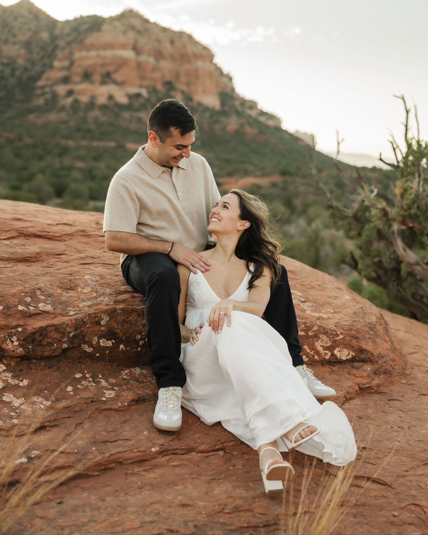 A couple shares intimate moments on red rocks with mountain views in the background.