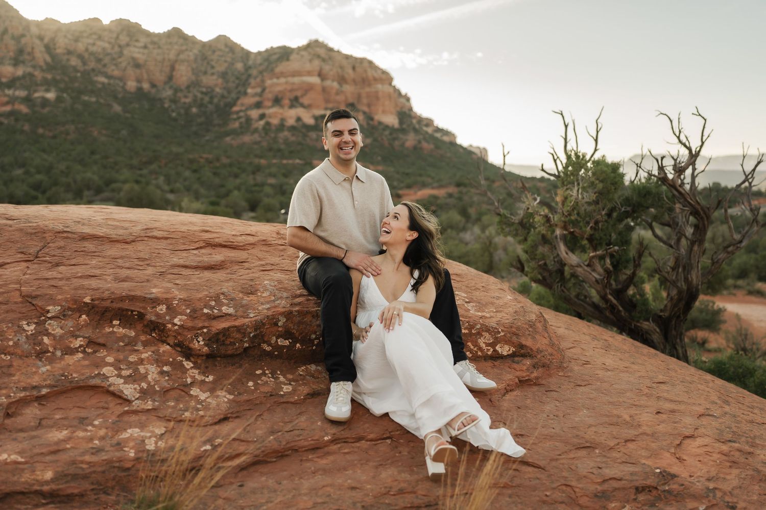Couple shares intimate moment on red rock formations during desert sunset.