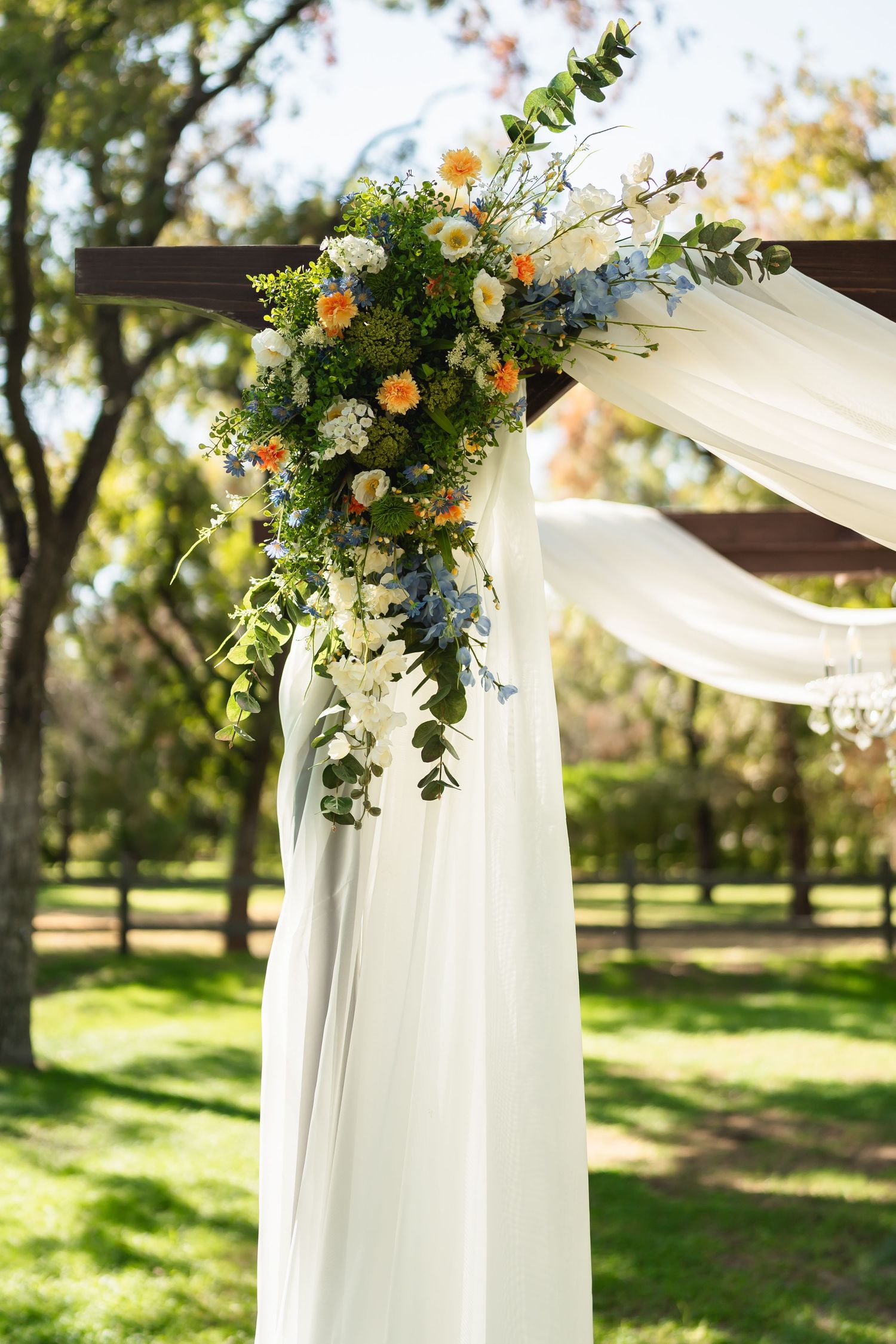 White fabric wedding arch decorated with peach and cream floral arrangements in an outdoor garden setting.
