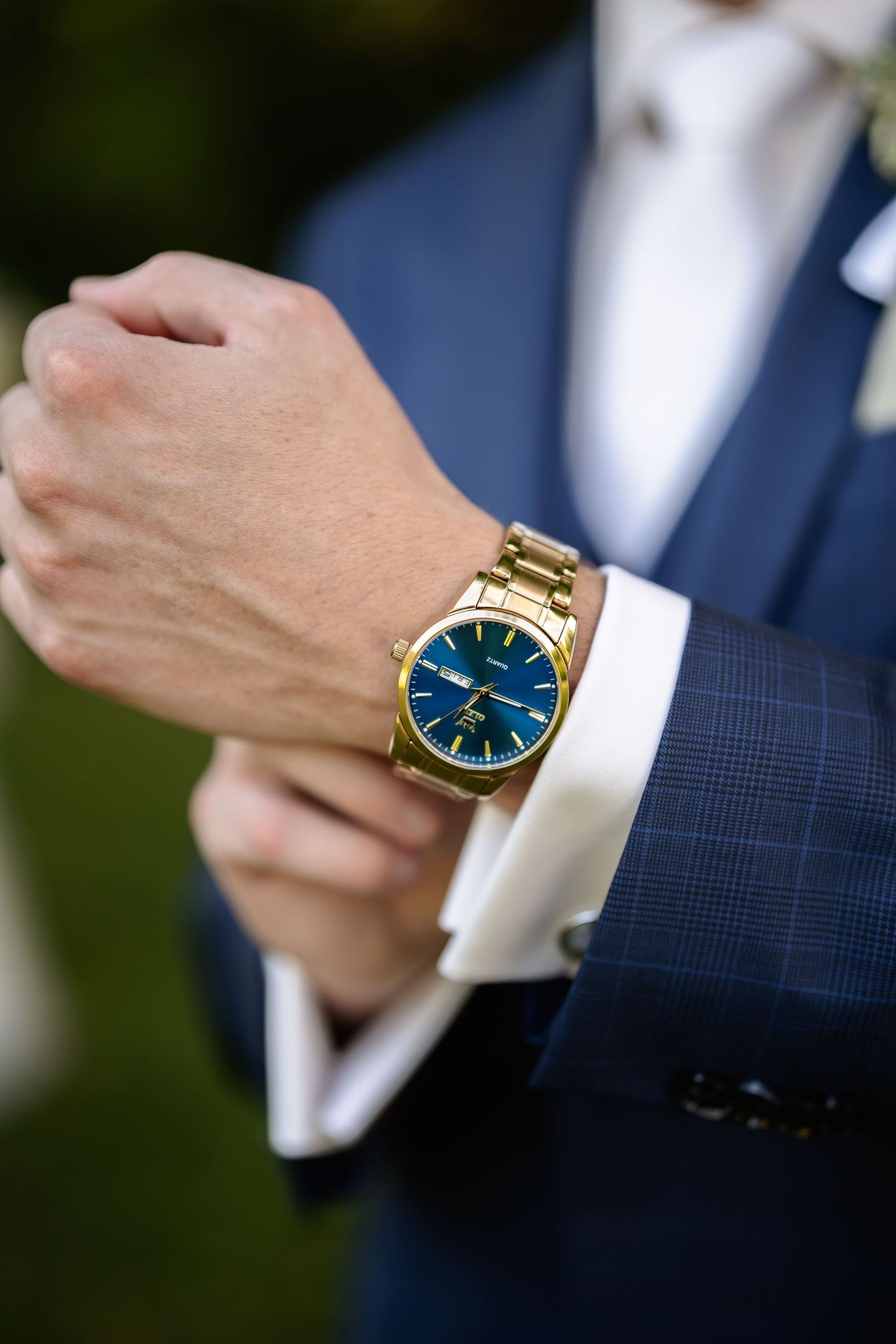 Close-up of gold watch with blue face on groom's wrist in formal navy suit.