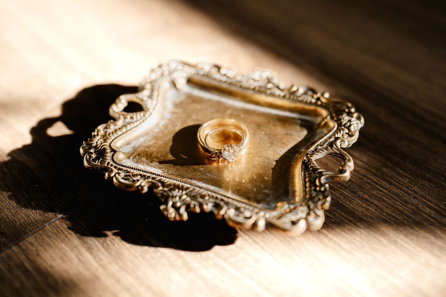 Vintage-style wedding rings photographed with dramatic lighting on ornate metal surface.