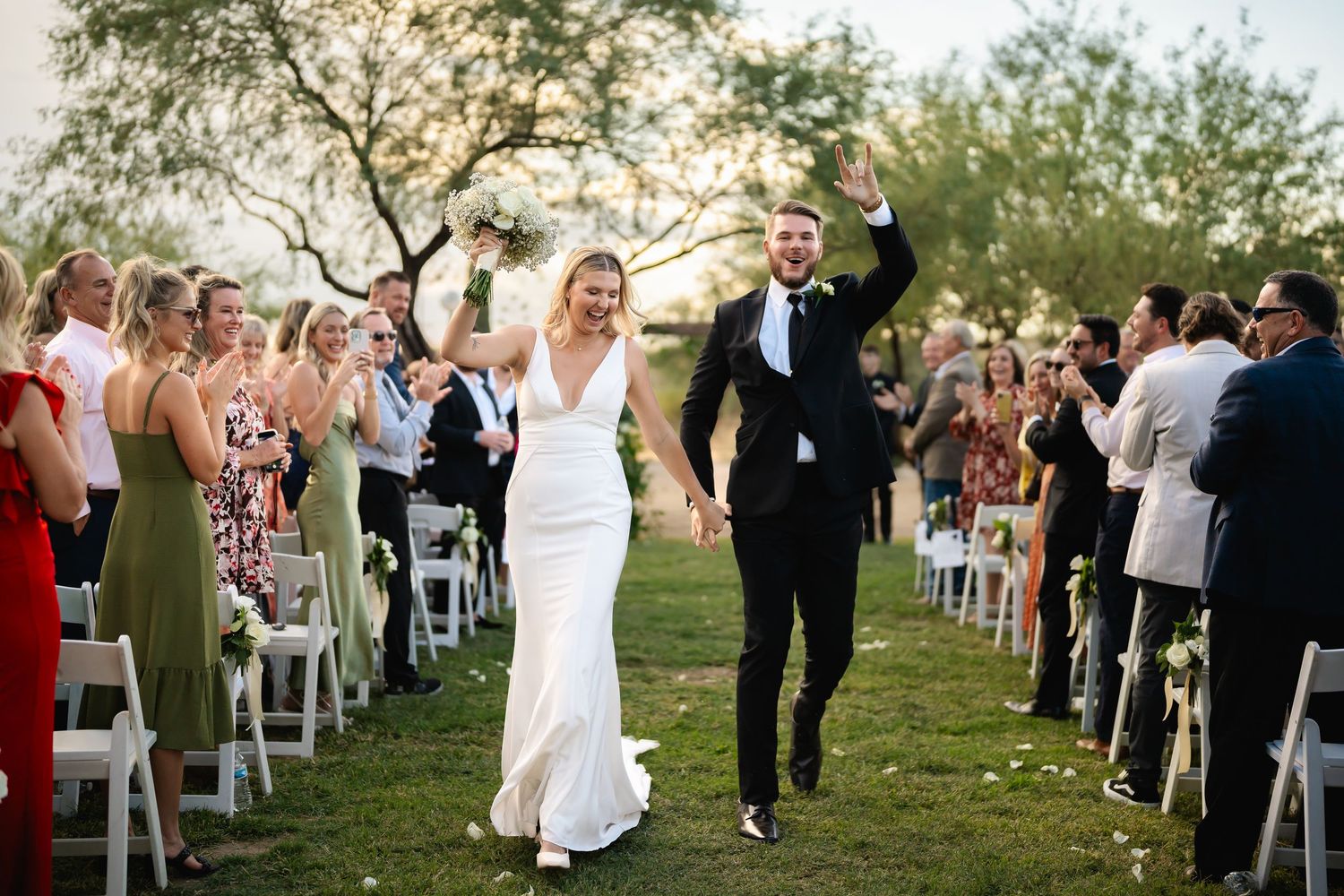 Wedding guests form a human tunnel outdoors with raised arms for the newlyweds to walk through during celebration.