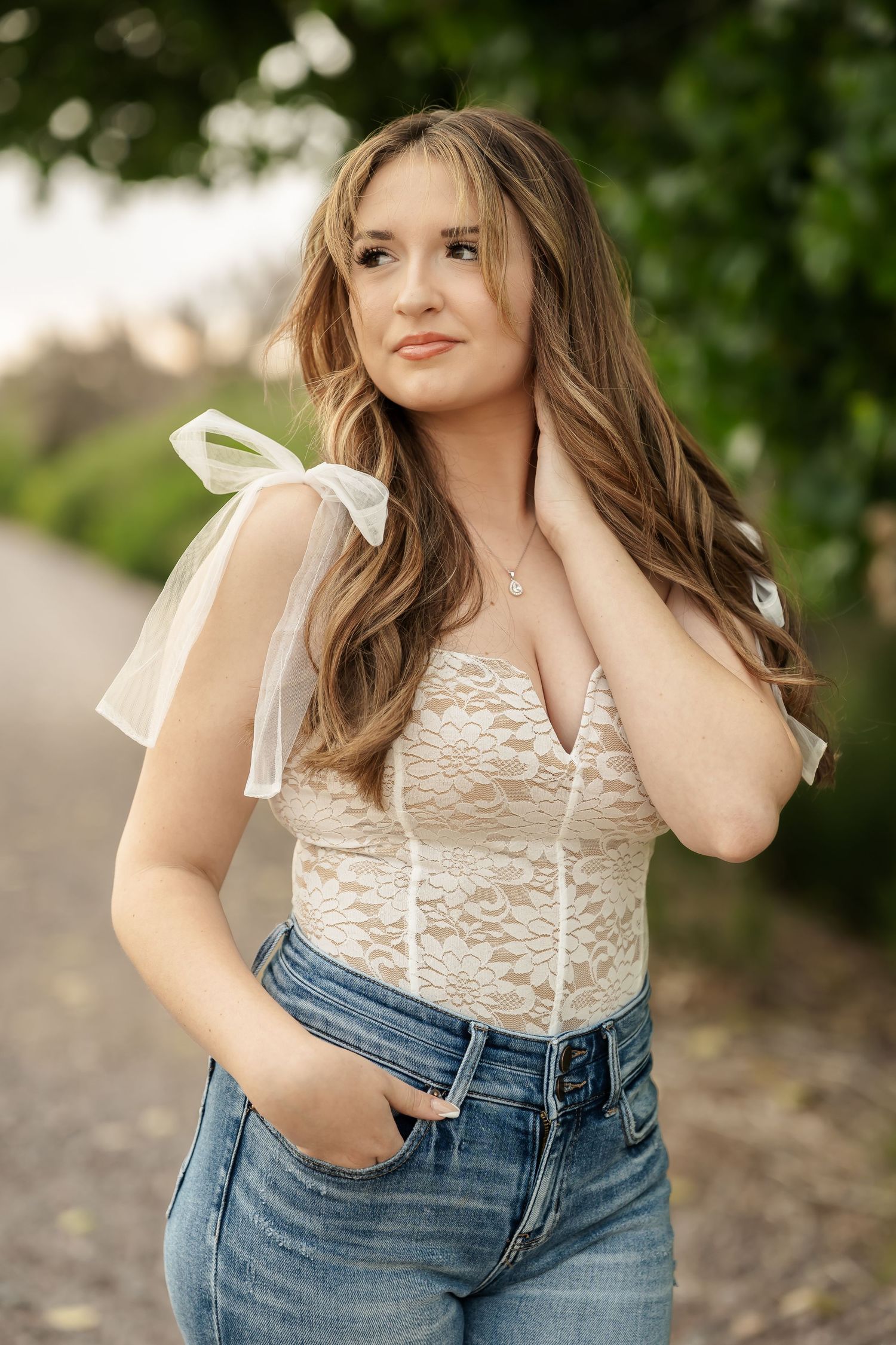 Person in white lace top and denim poses outdoors in natural lighting.