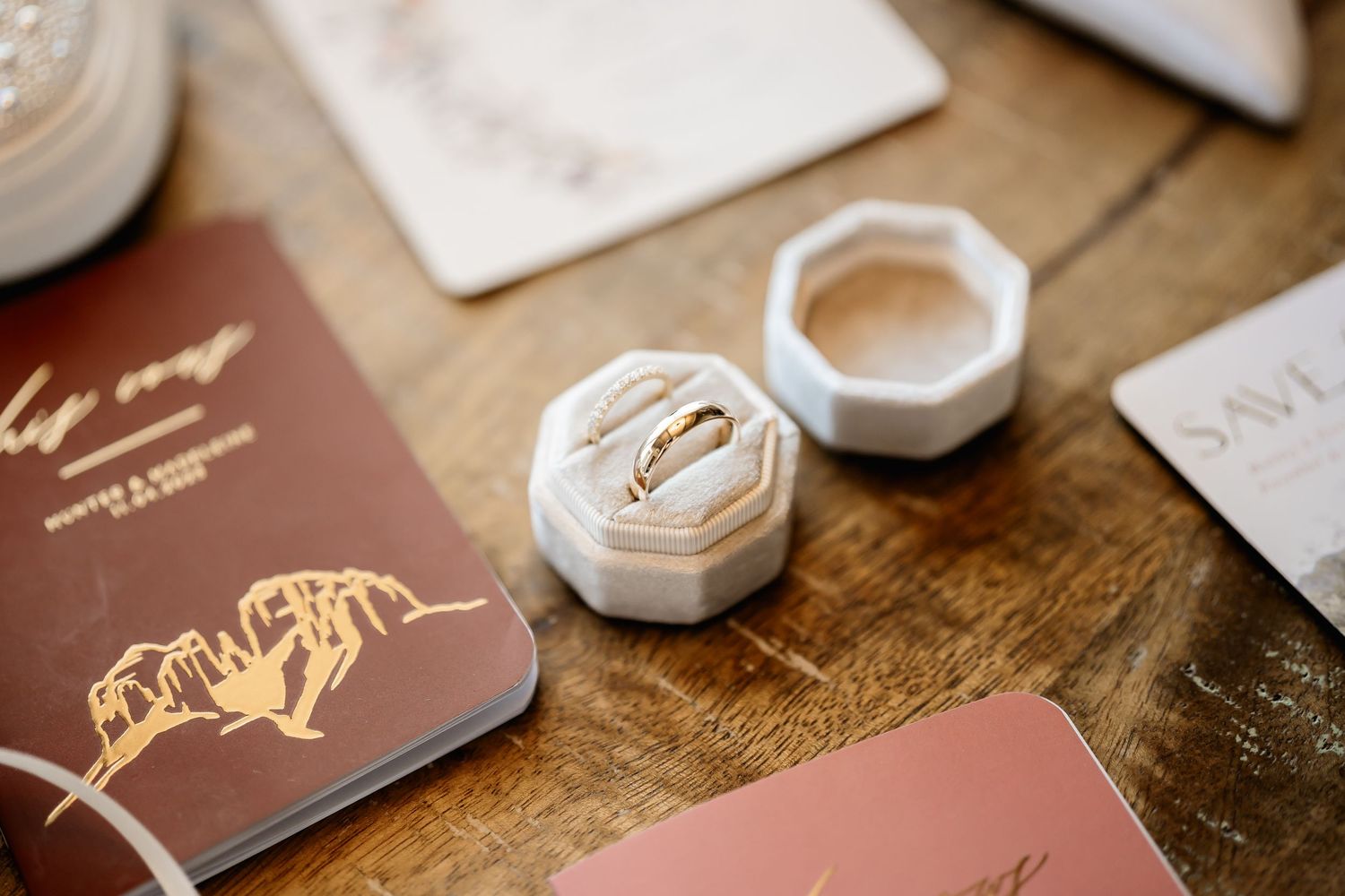Wedding rings and decor items arranged on a rustic wooden surface with small wedding photo albums nearby.