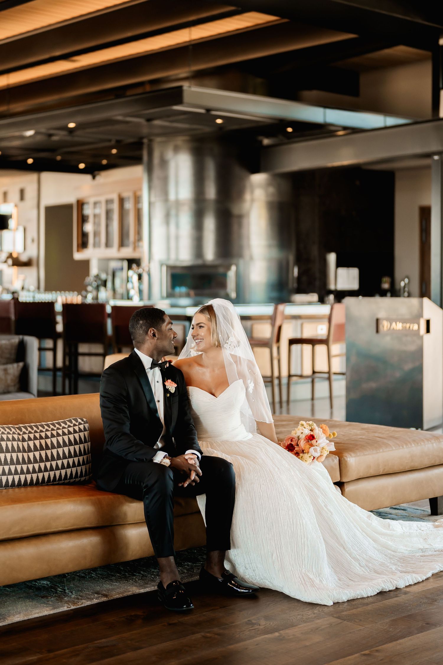 Wedding couple seated on modern lounge furniture in an elegant indoor setting.