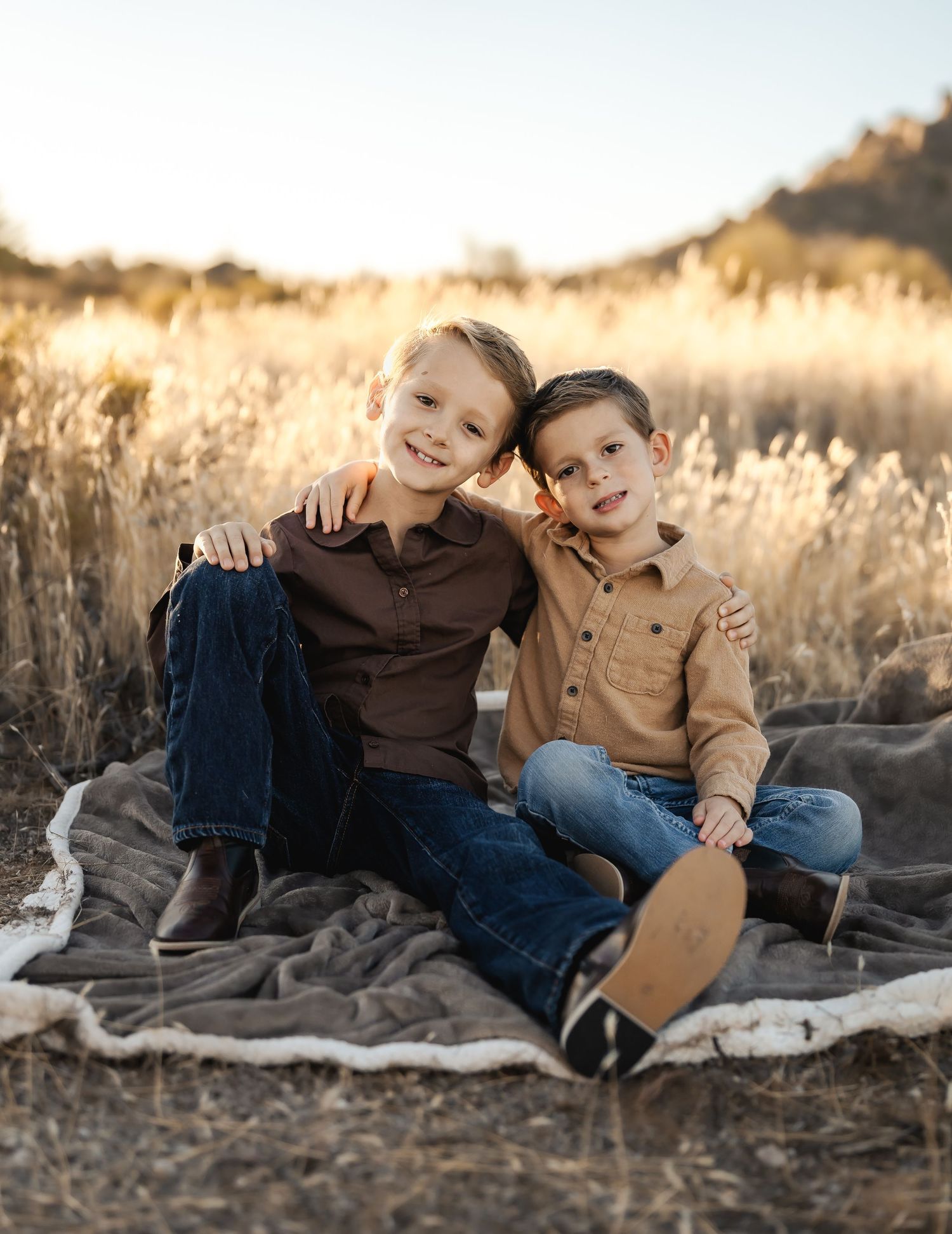 Two young children laughing together on blanket in golden field at sunset.