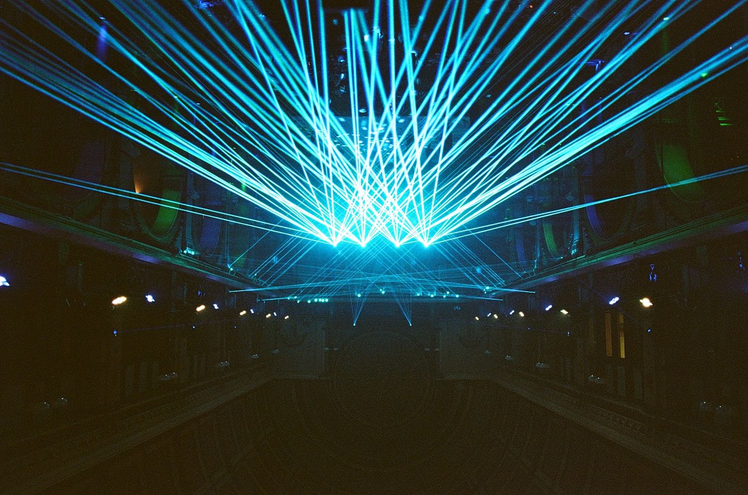 Spectacular blue laser light show with radiating beams illuminating a dark concert venue or event space.