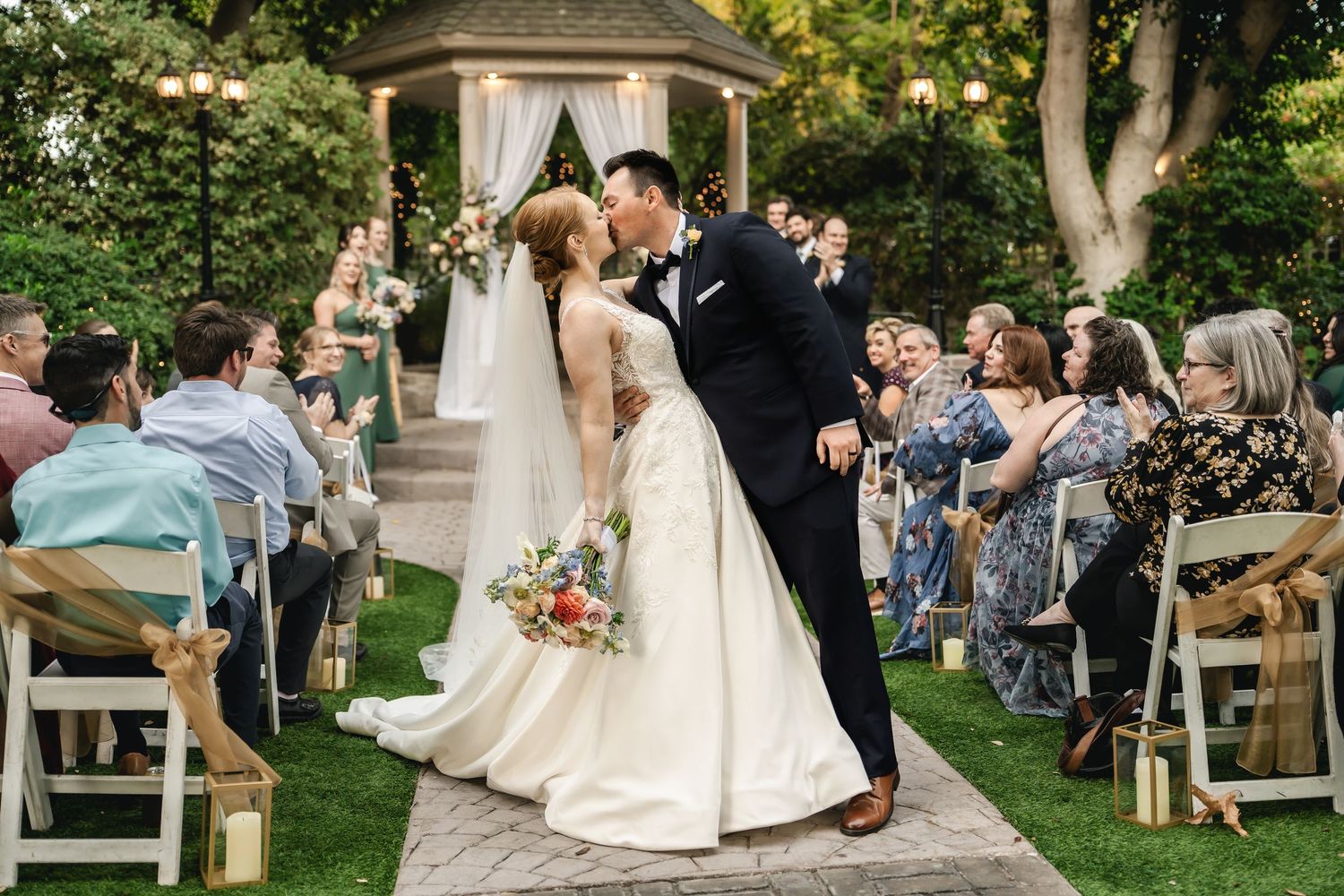 Intimate outdoor wedding ceremony moments captured in a lush garden setting with a wooden gazebo and natural lighting.