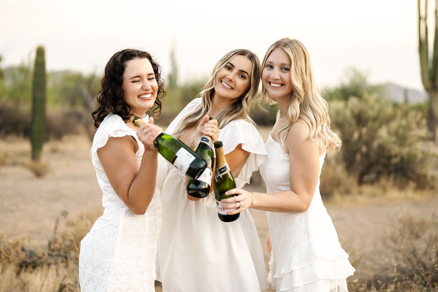 Friends enjoying wine and laughter together among towering saguaro cacti at sunset.